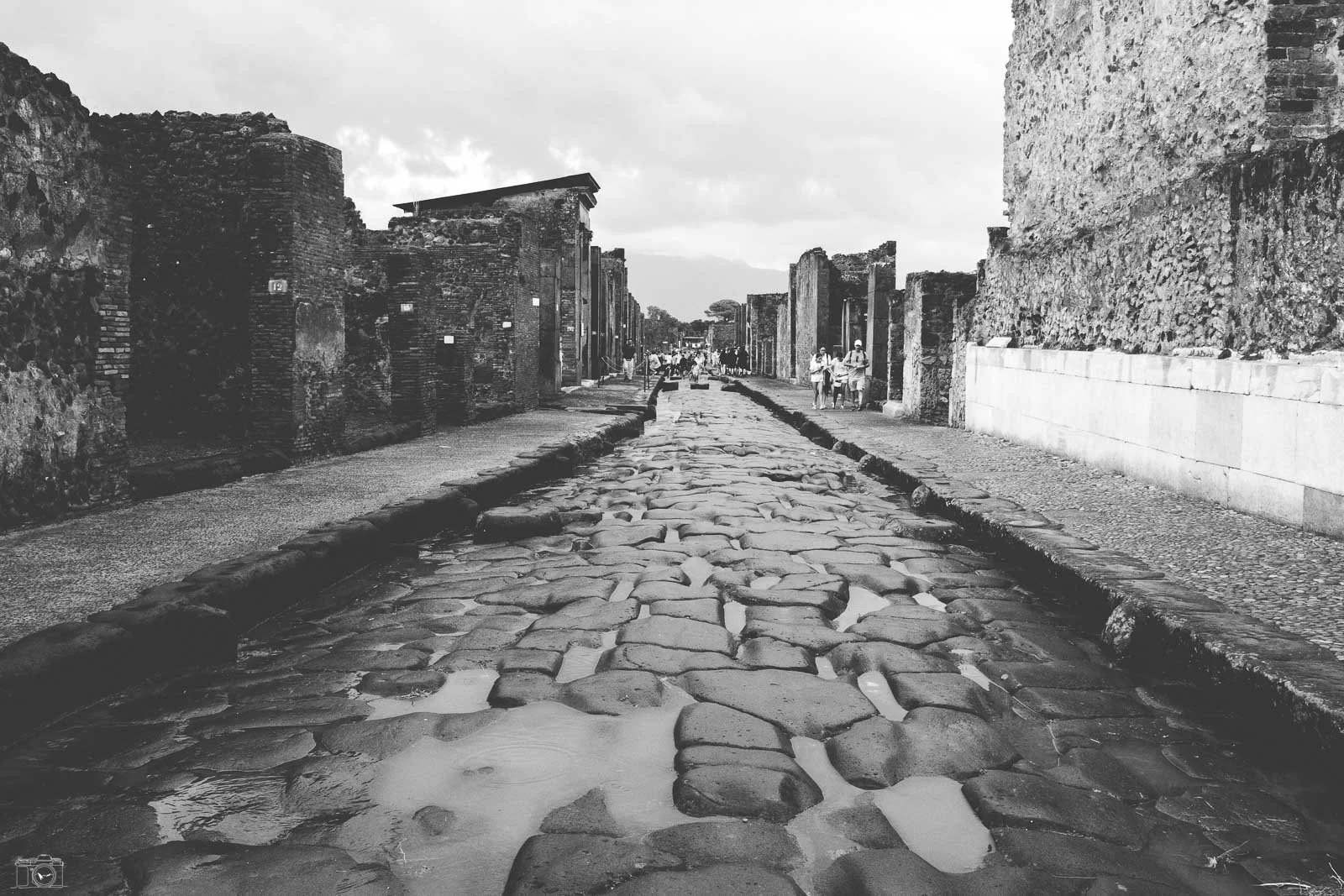 Voie pavée ancienne dans une ruine historique avec des murailles en pierre et des touristes qui explorent le site.