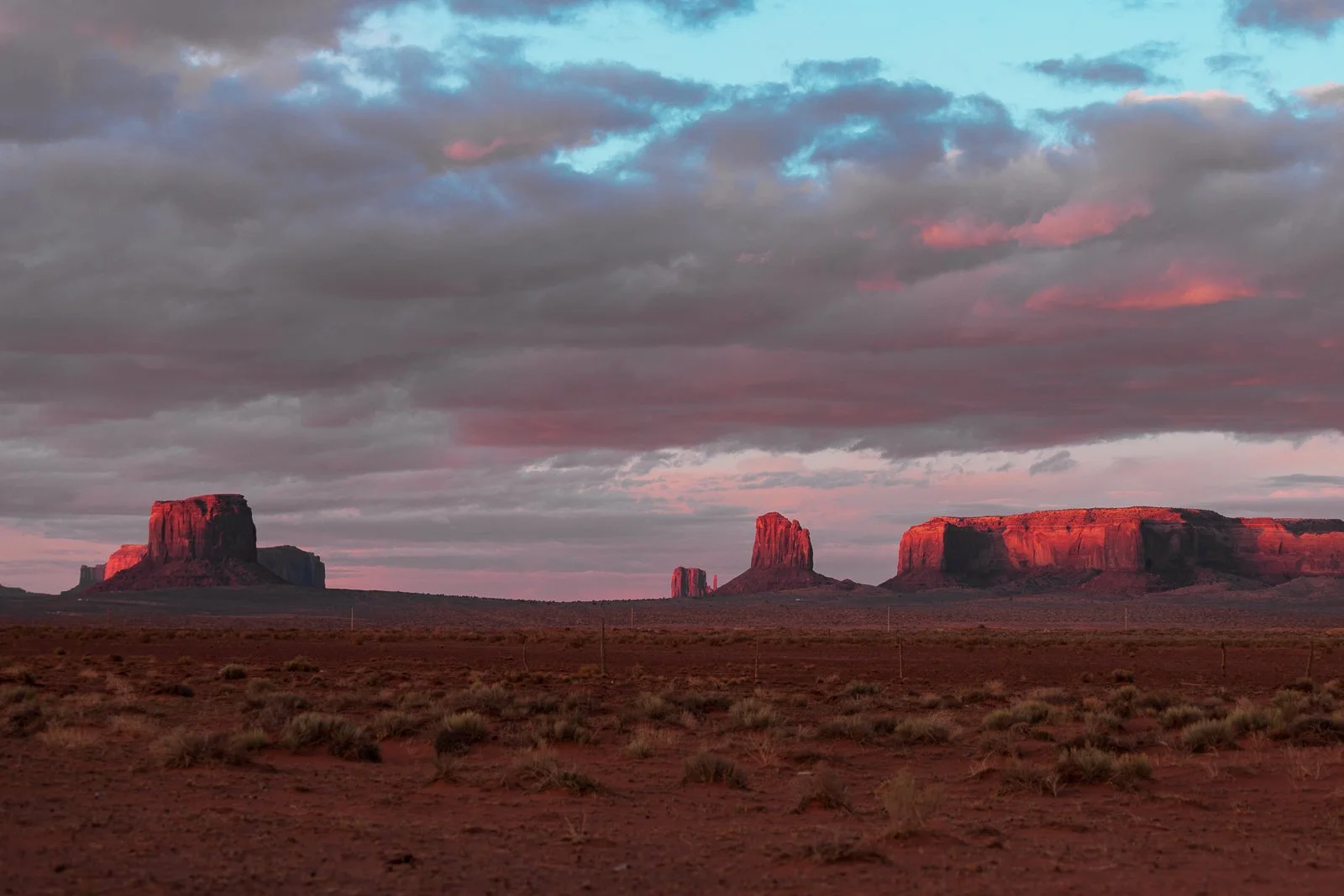 Paysage désertique avec des formations rocheuses rouges sous un ciel nuageux au crépuscule.