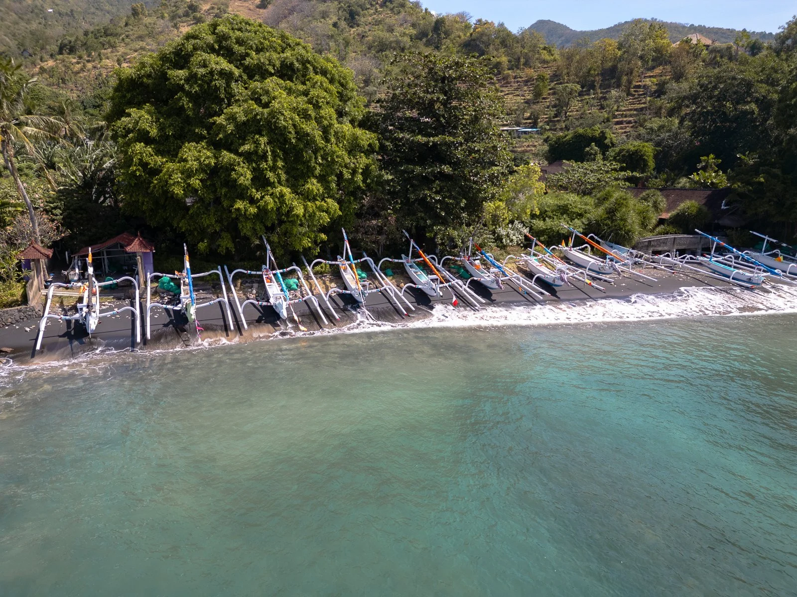 Vue aérienne de bateaux de pêche traditionnels alignés sur une plage avec de la végétation luxuriante en arrière-plan