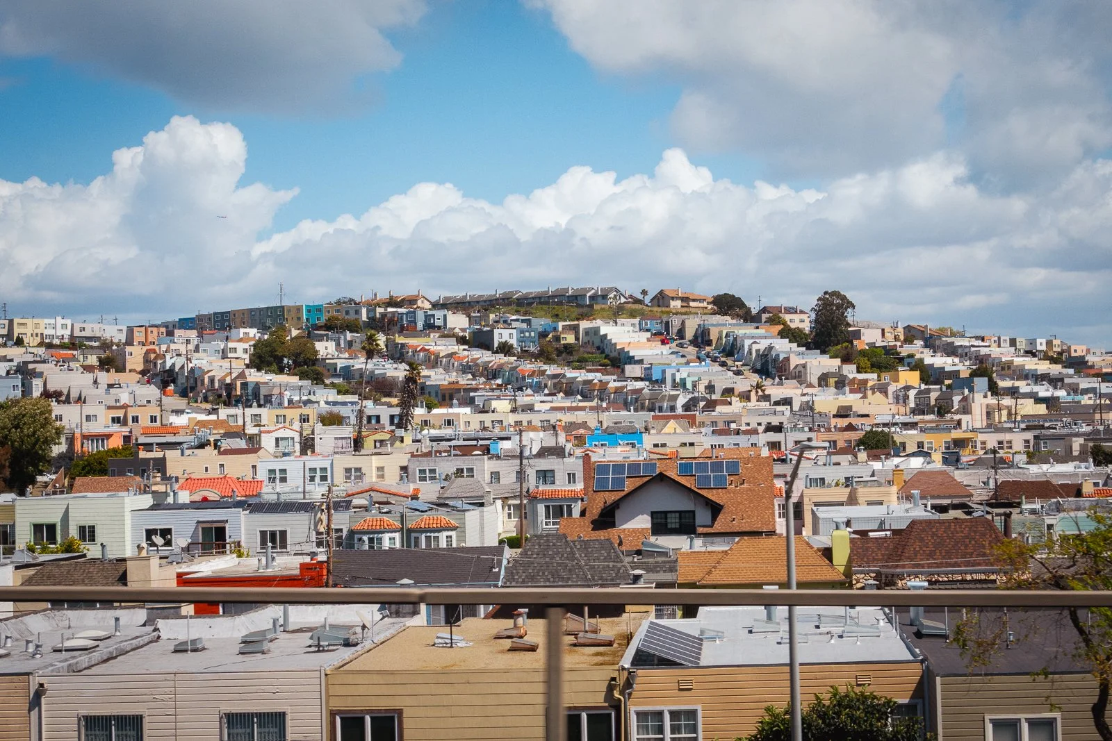 Ville résidentielle avec de nombreux maisons colorées et toit de différentes couleurs et matériaux, montagnes au fond, ciel partiellement nuageux.