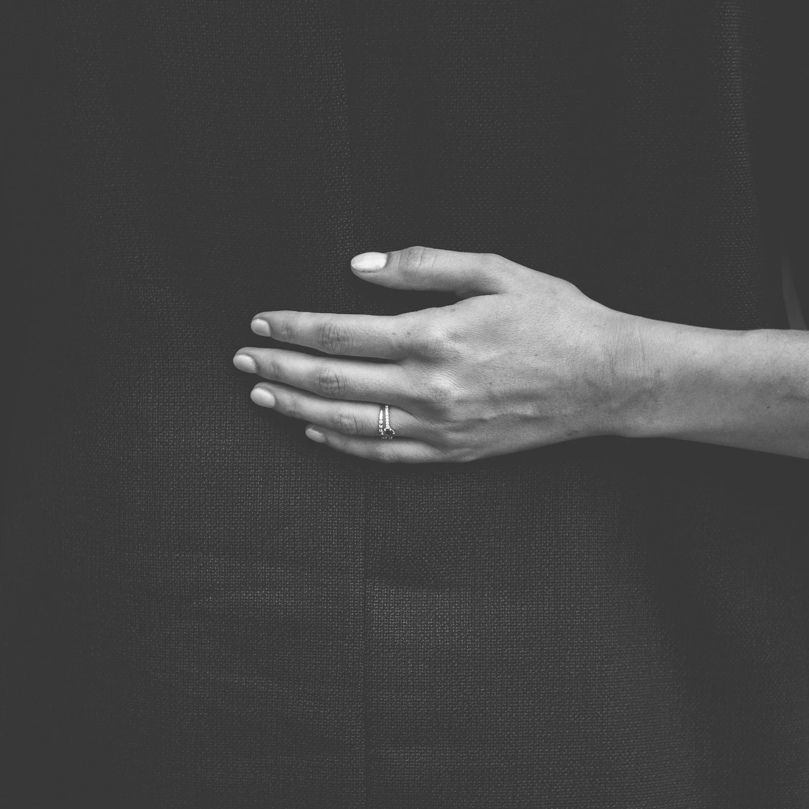 Une main féminine posée sur le ventre d'une personne portant une robe noire, portant une bague à l'annulaire.