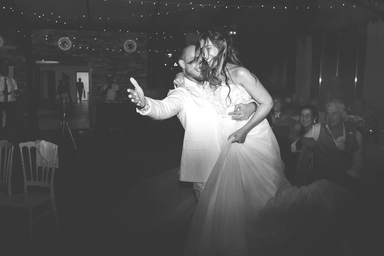 Un couple danse lors d'un mariage, la mariée en robe blanche et le marié en costume clair.
