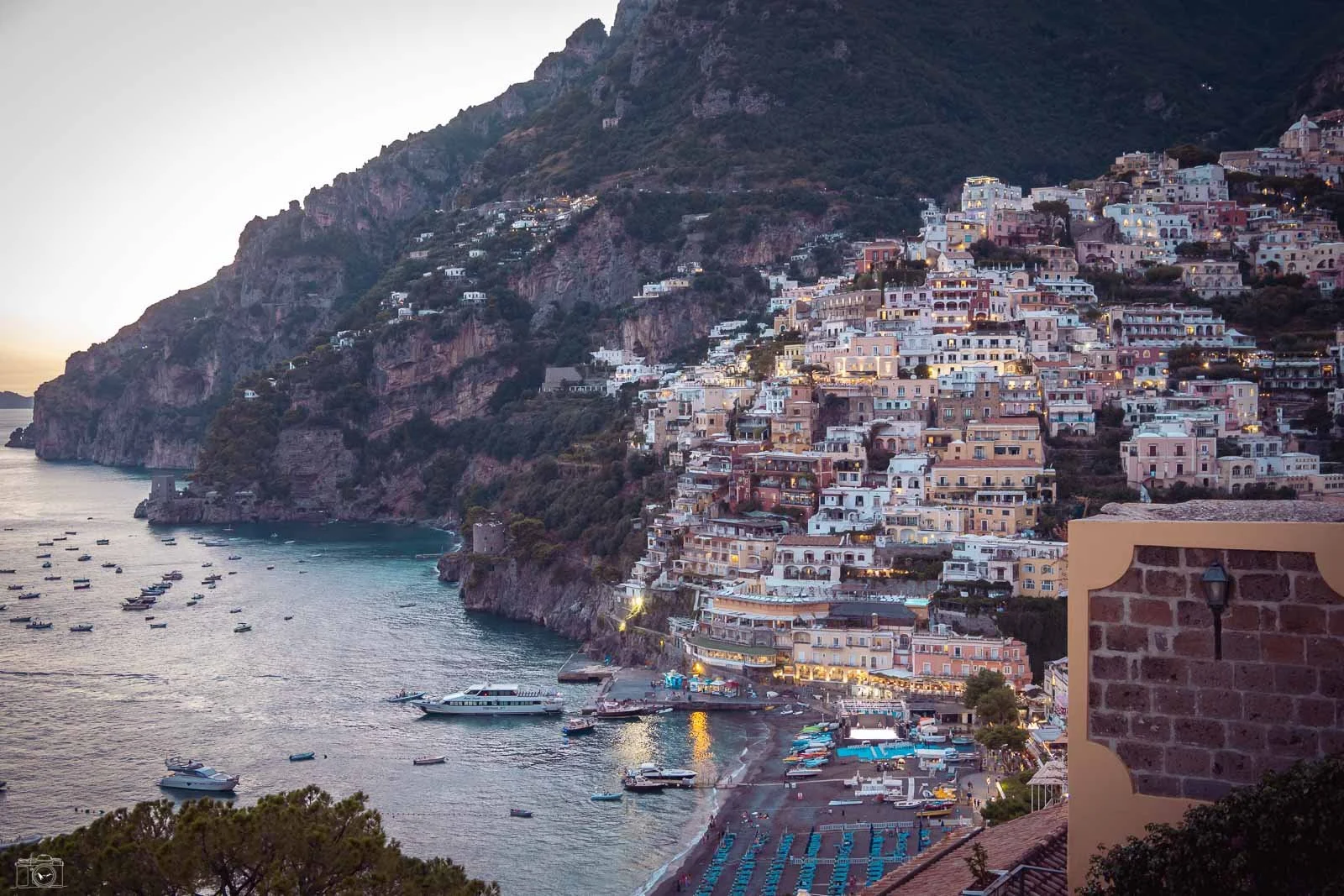 Vue de la côte rocheuse avec une ville en terrasses construite sur la montagne, face à la mer, avec plusieurs bateaux dans l'eau.