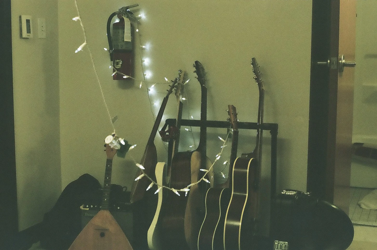 Group of guitars leaning against a wall decorated with string lights and a fire extinguisher.