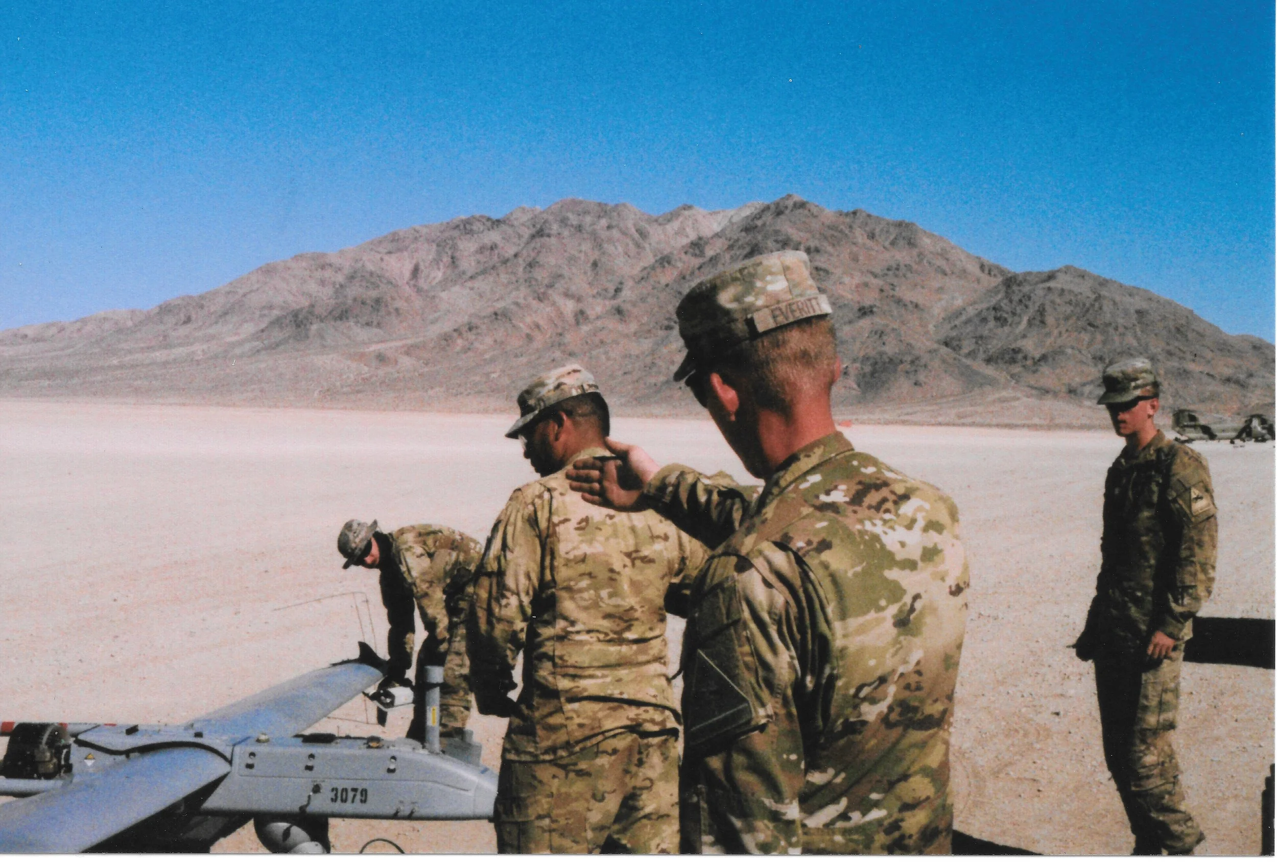 Military personnel preparing a drone in a desert landscape with mountains in the background.