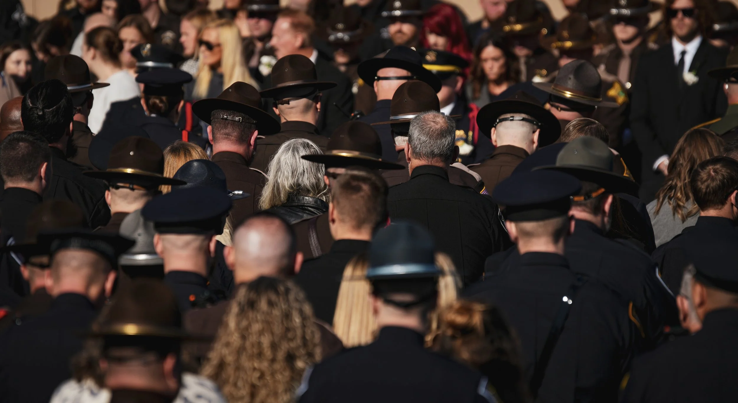 Crowd of people, including police officers in uniform with hats, gathered outdoors for a ceremony or event.