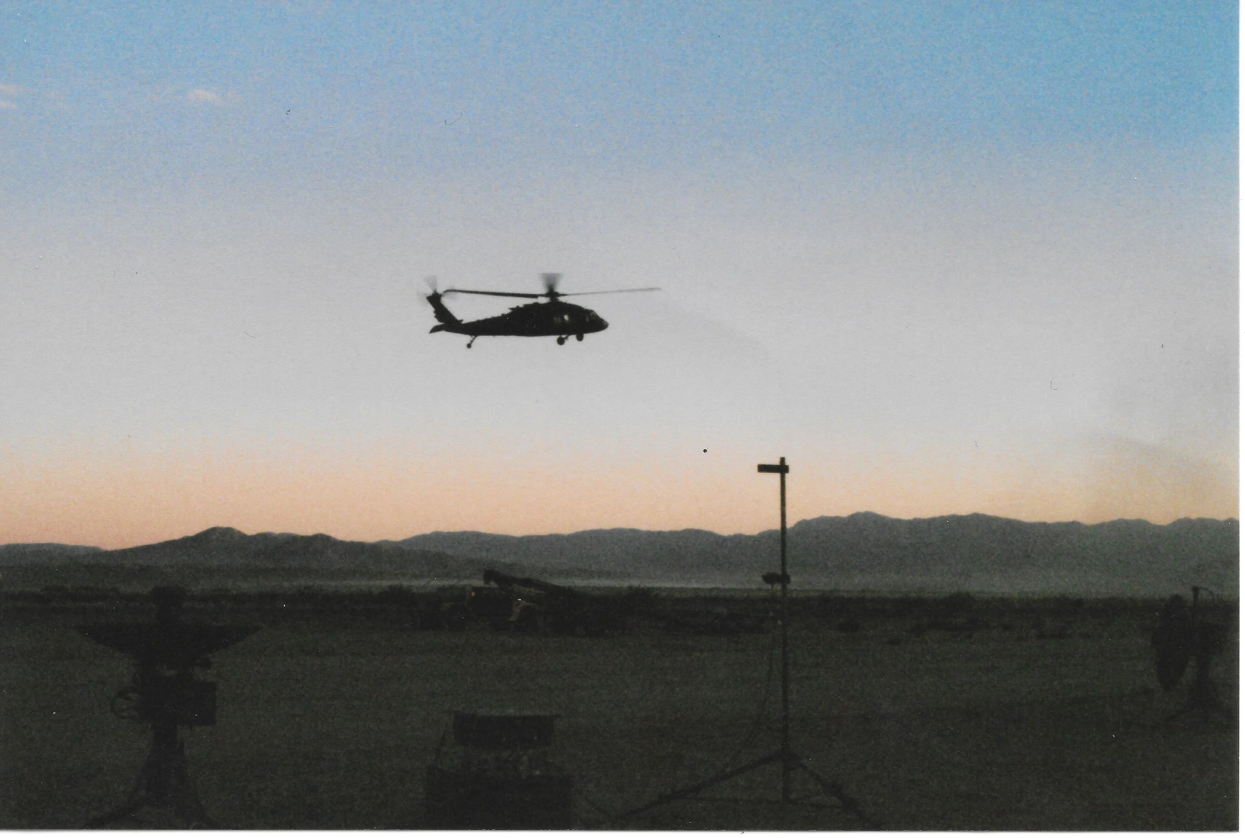 Silhouette of a helicopter flying in the sky during sunset with mountains and a signpost in the foreground.