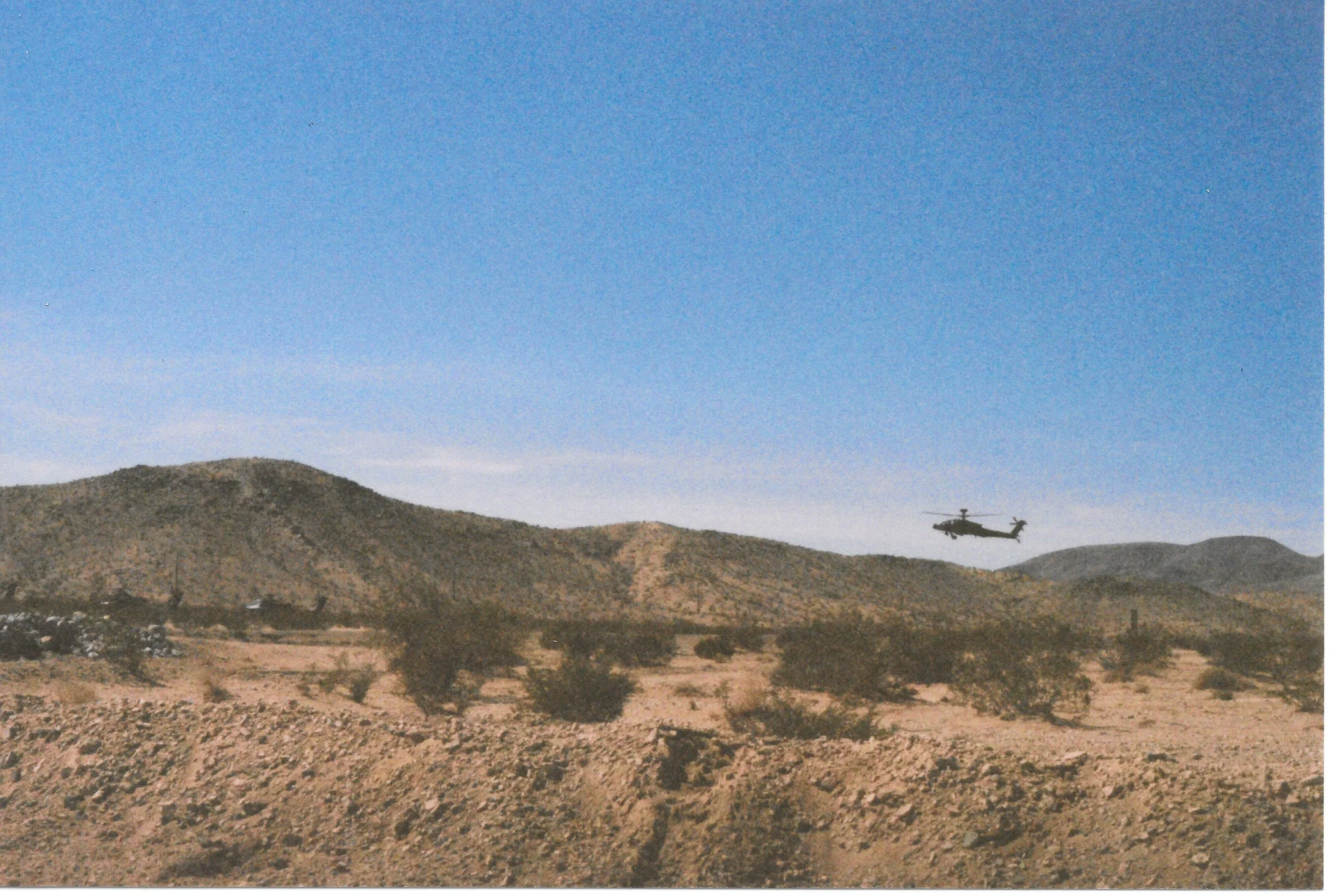 A helicopter flying over a dry, mountainous landscape with clear blue sky.