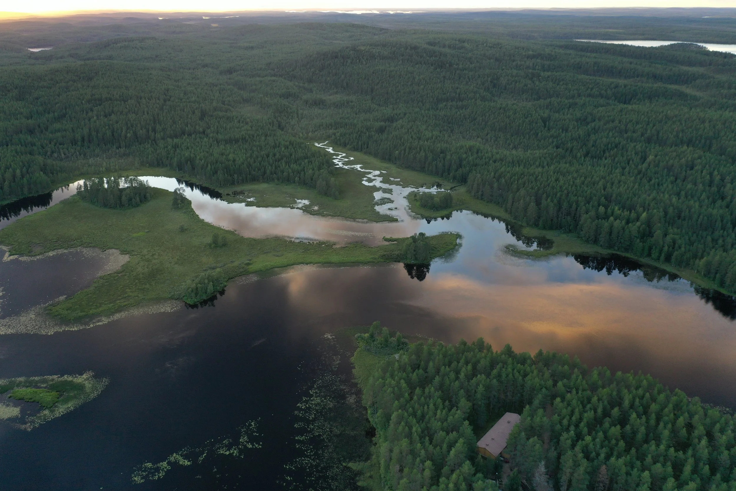 An aerial view of a large lake surrounded by dense green forest, with several smaller water bodies and a building nestled among the trees.