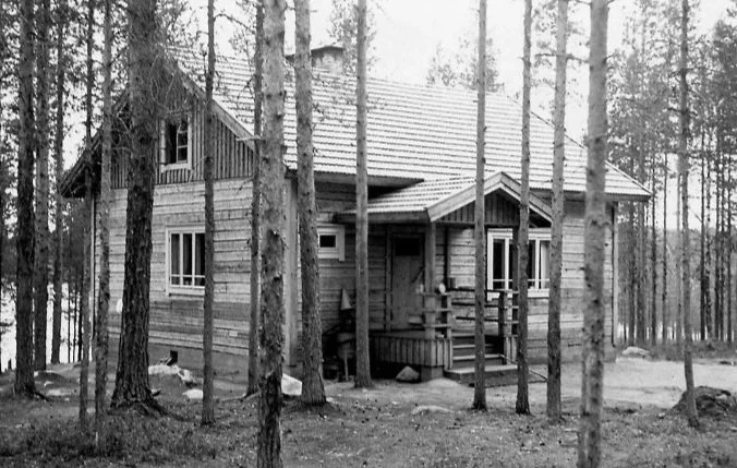A small wooden house in a wooded area with tall trees surrounding it.