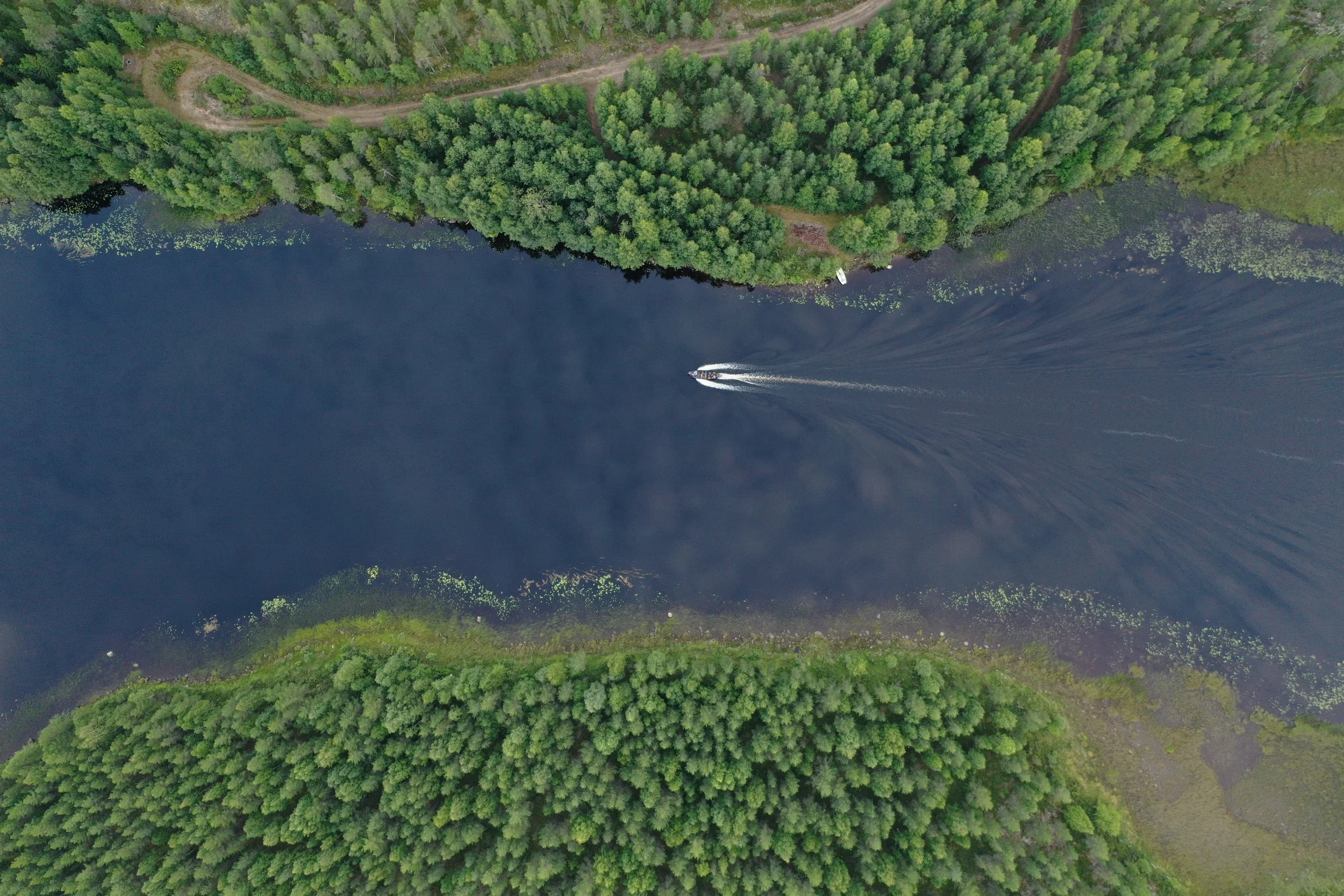 Aerial view of a boat moving on a dark blue river with green trees on both sides.