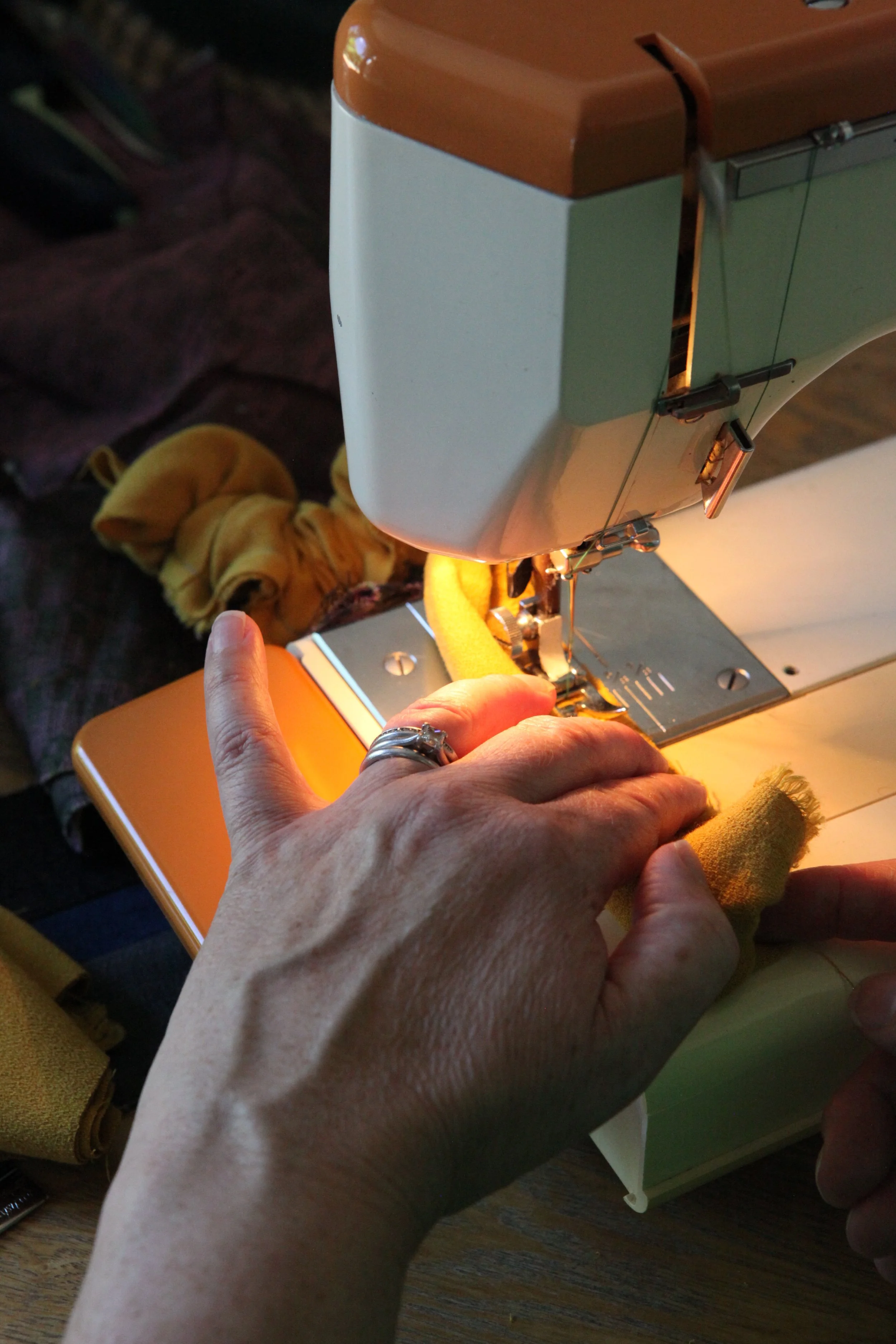 Close-up of a person's hands operating a vintage sewing machine, with a yellow fabric in the process of being sewn, in a cozy, indoor setting.