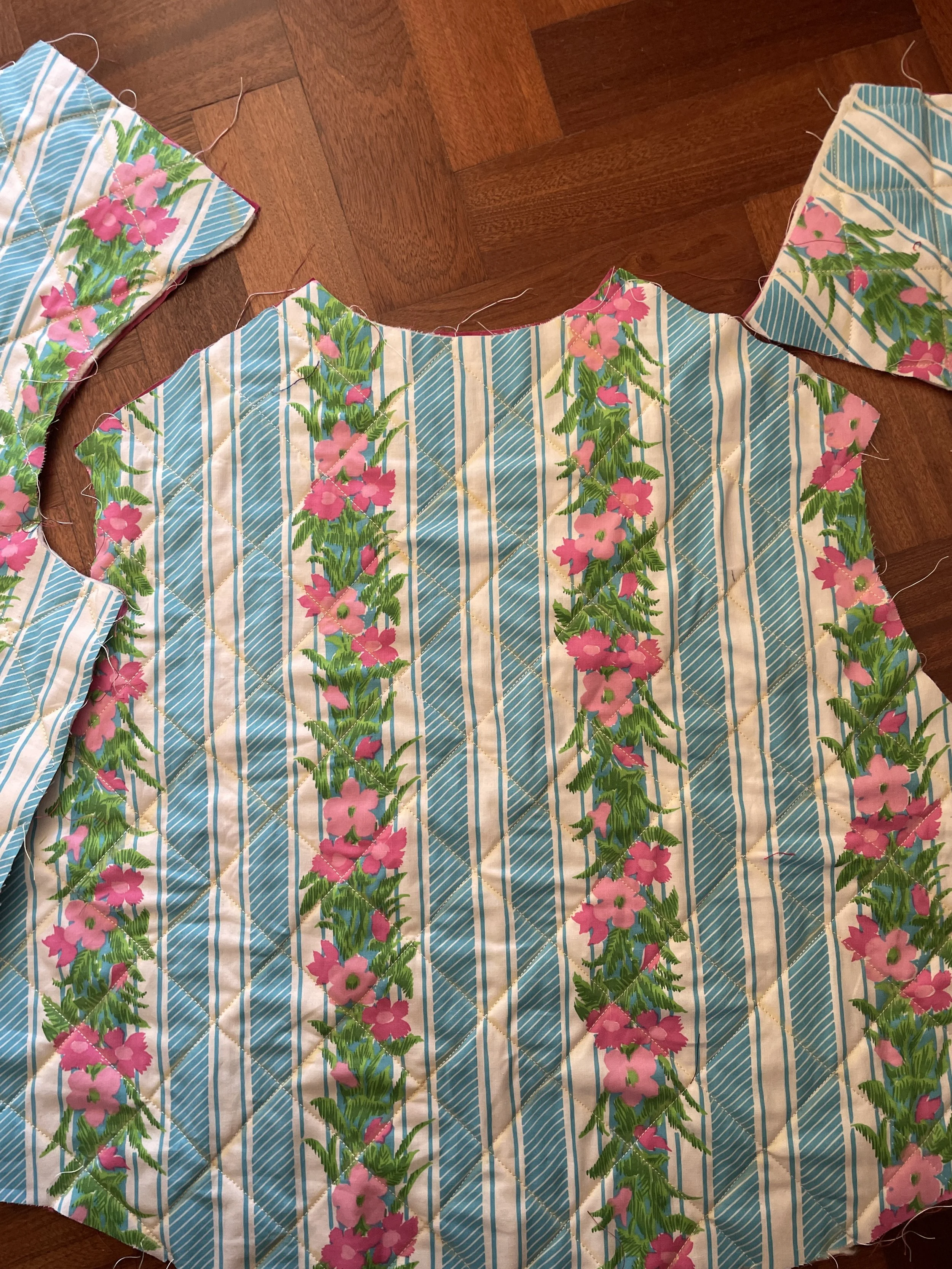 A floral patterned fabric with green, pink, and blue colors, partially sewn with edges visible, laid out on a wooden floor.