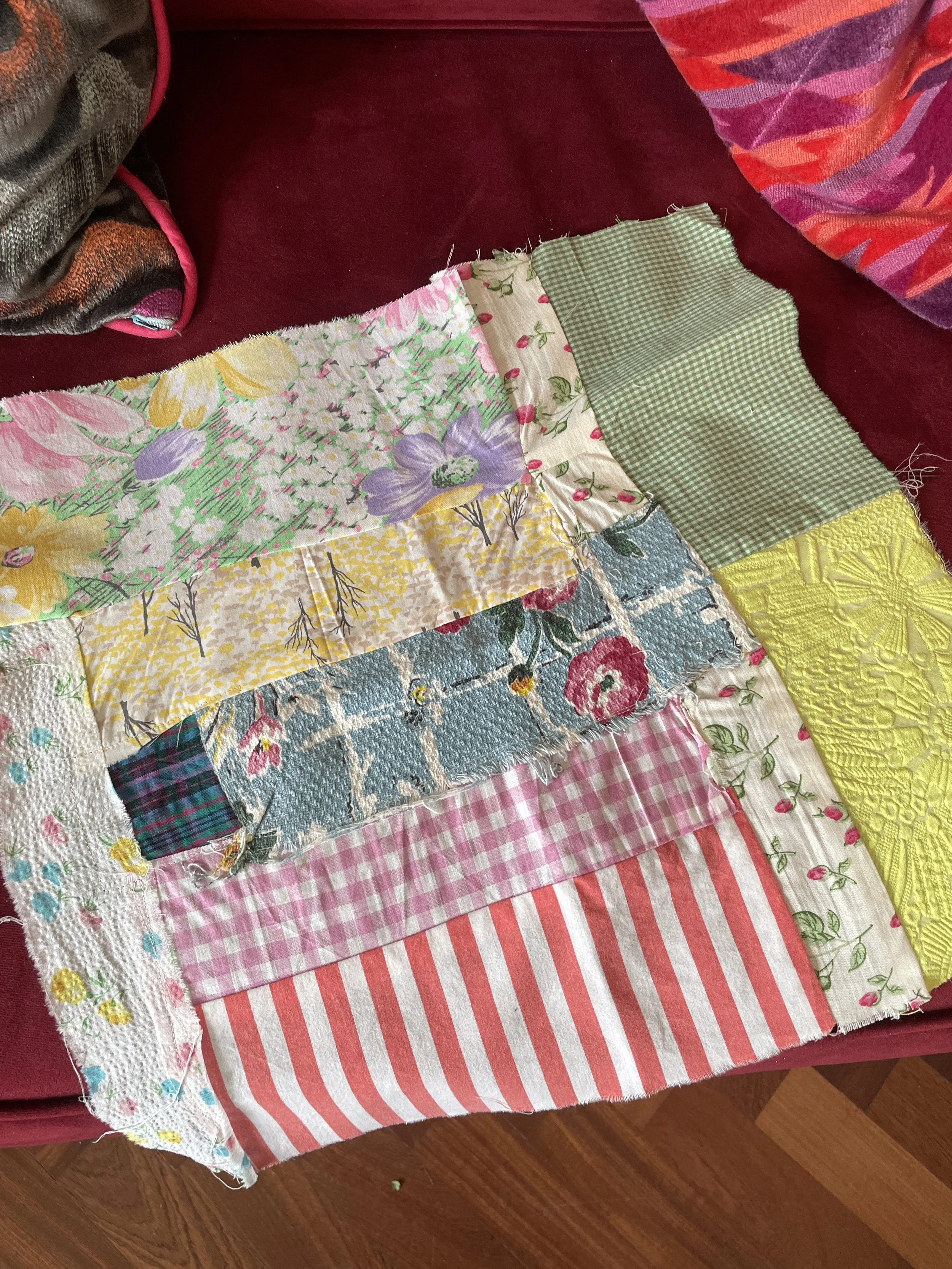 Patchwork quilt with various colorful fabric patterns, including floral, gingham, and striped, lying on a wooden floor.