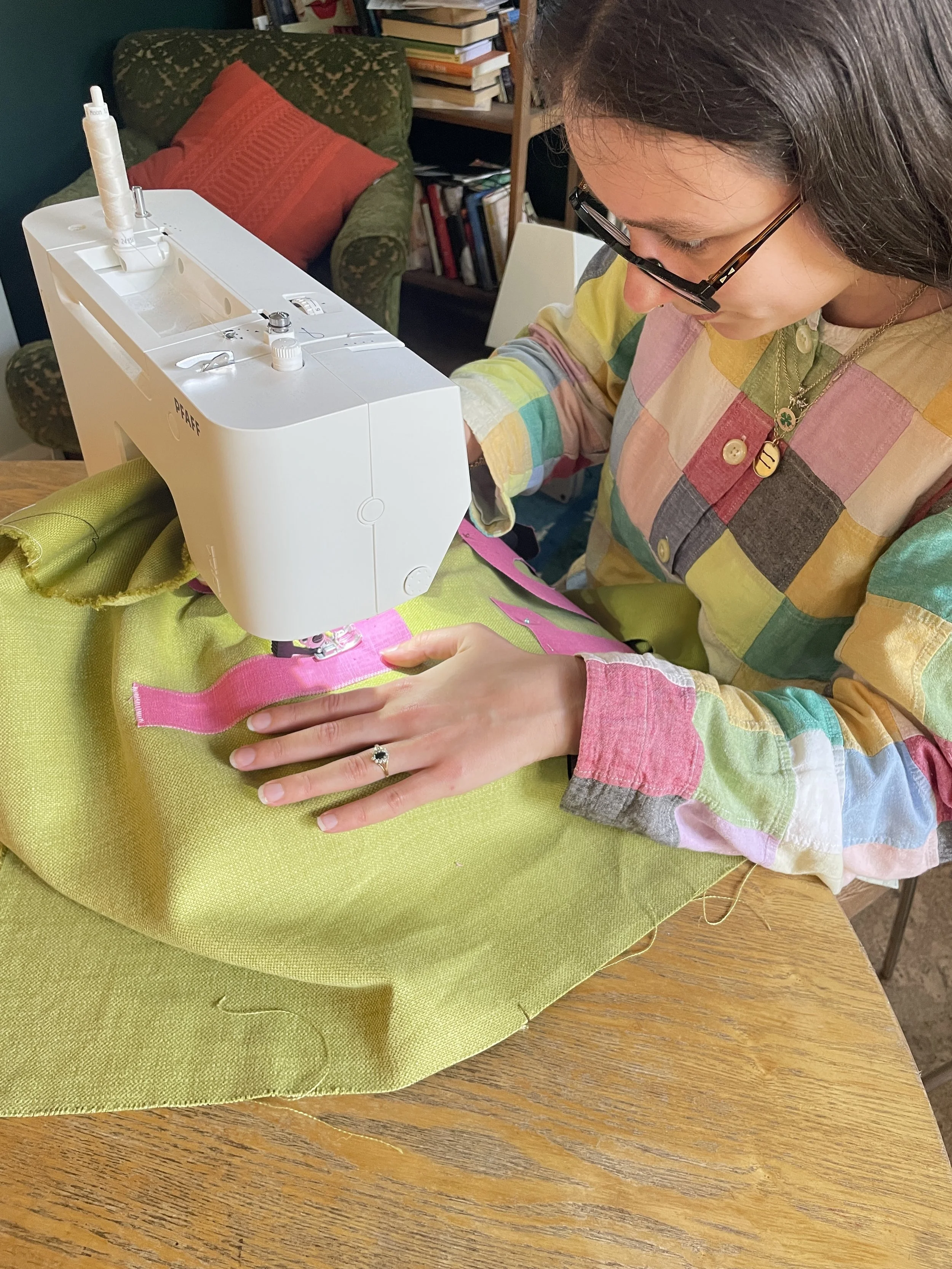 A woman using a sewing machine to stitch pink fabric onto green fabric on a wooden table.