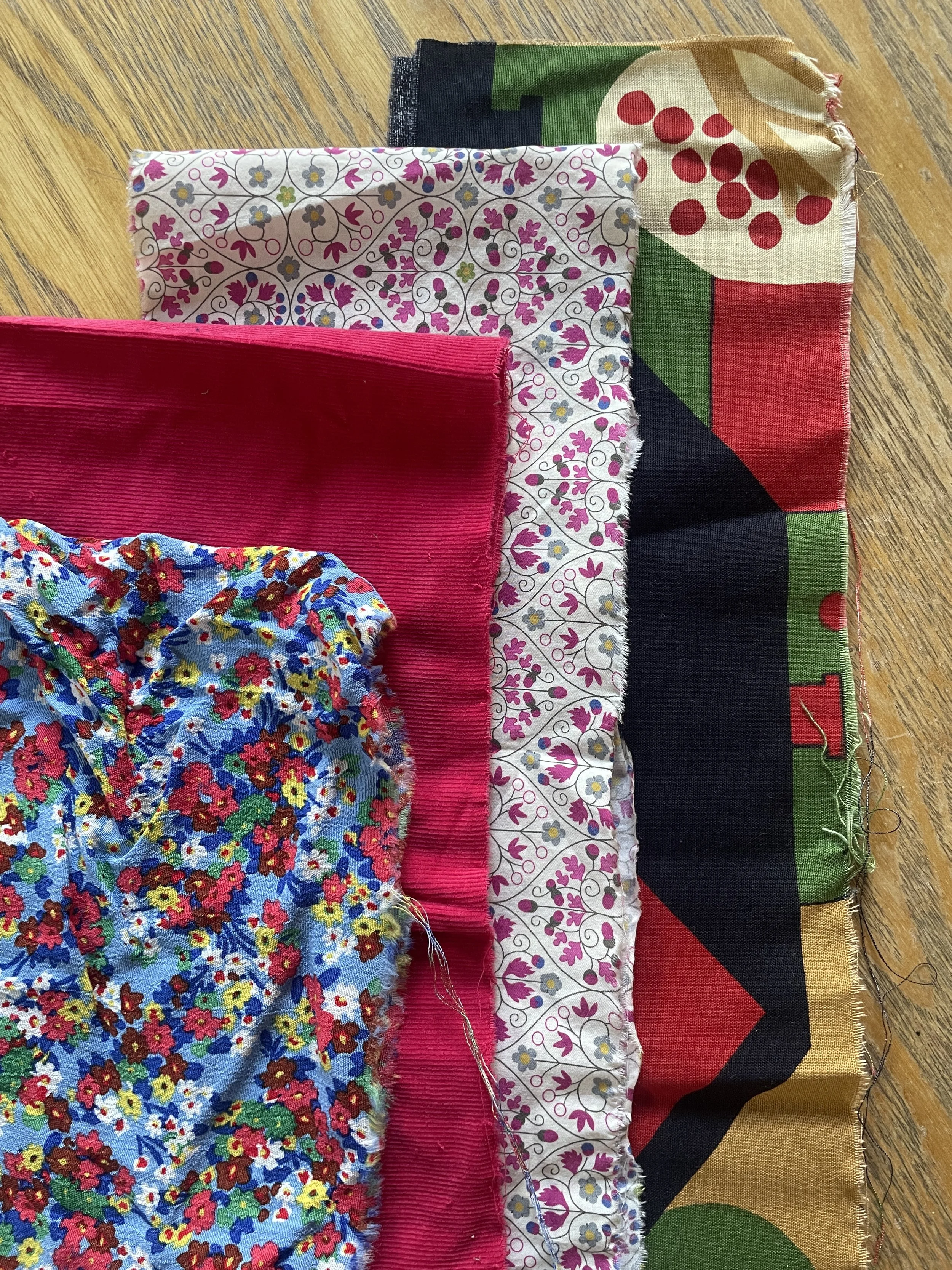 Various colorful fabric pieces with floral and abstract patterns layered on a wooden surface.