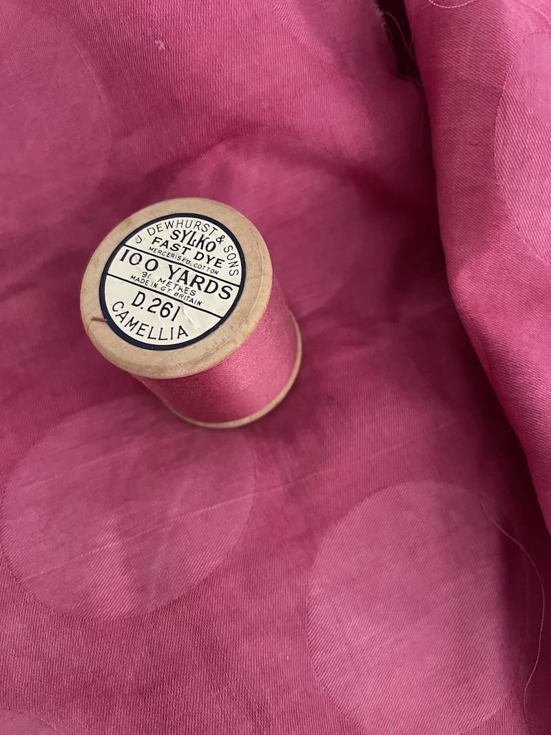 A spool of pink silk sewing thread placed on pink fabric with a circular pattern.