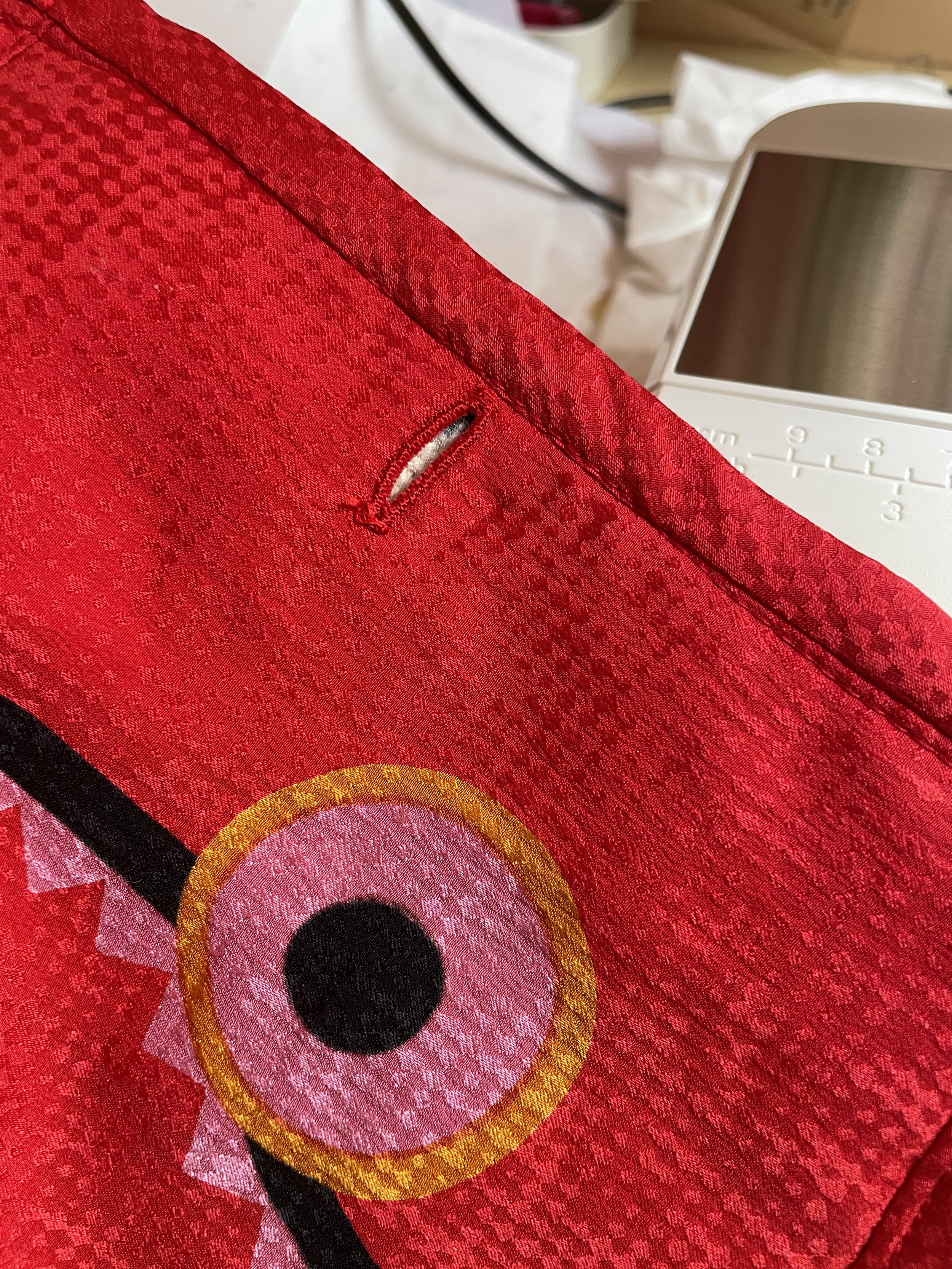 Close-up of a colorful printed silk fabric with a button hole showing, bound at the edges with bias binding. 