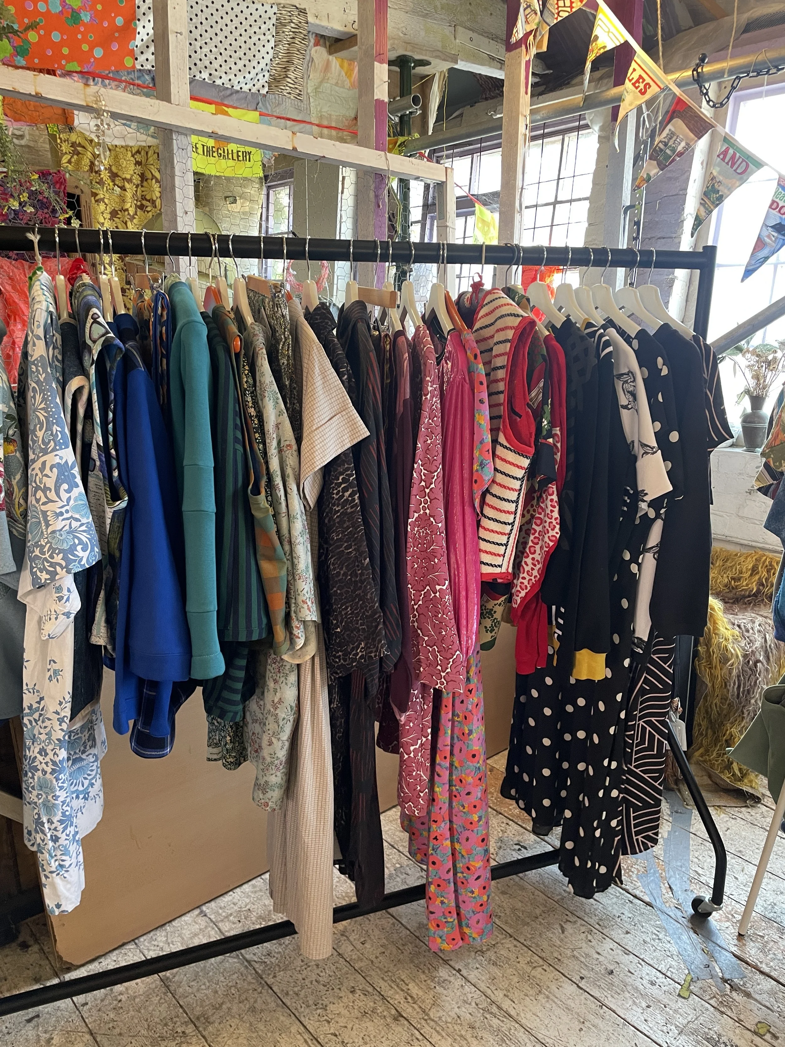 A clothing rack with various patterned and solid-colored shirts and dresses in a vintage or thrift store setting.