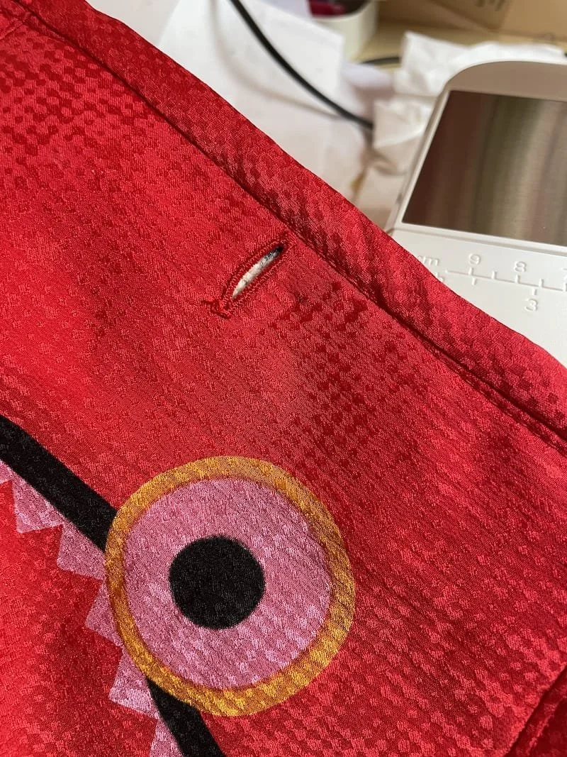 Close-up of a colorful printed silk fabric with a button hole showing, bound at the edges with bias binding. 