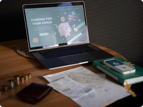 Laptop displaying a financial website about funding goals, placed on a wooden desk surrounded by papers, a wallet, and a calculator.