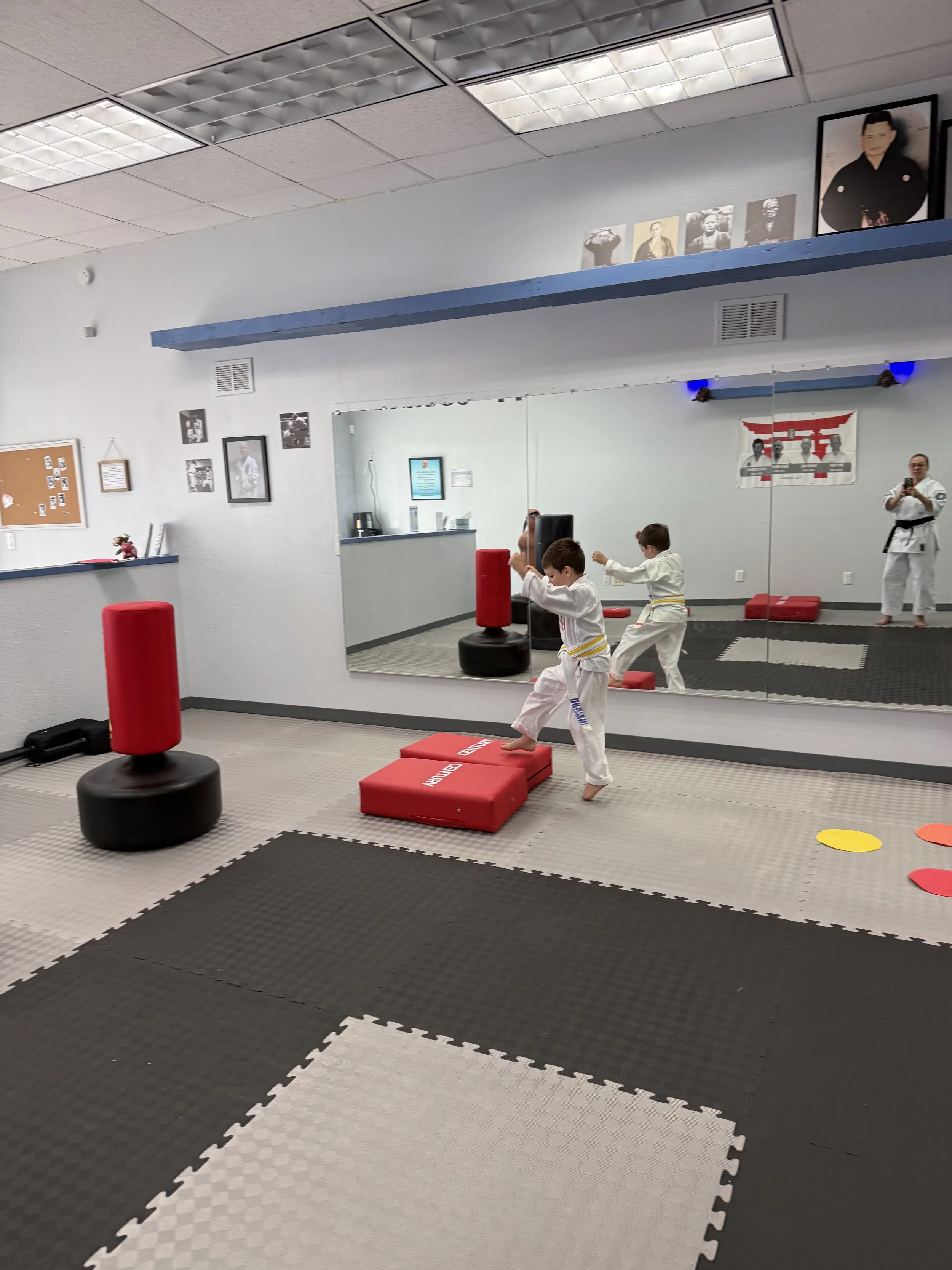 A martial arts training room with children practicing with punching bags, mirror, pictures, and decorations.