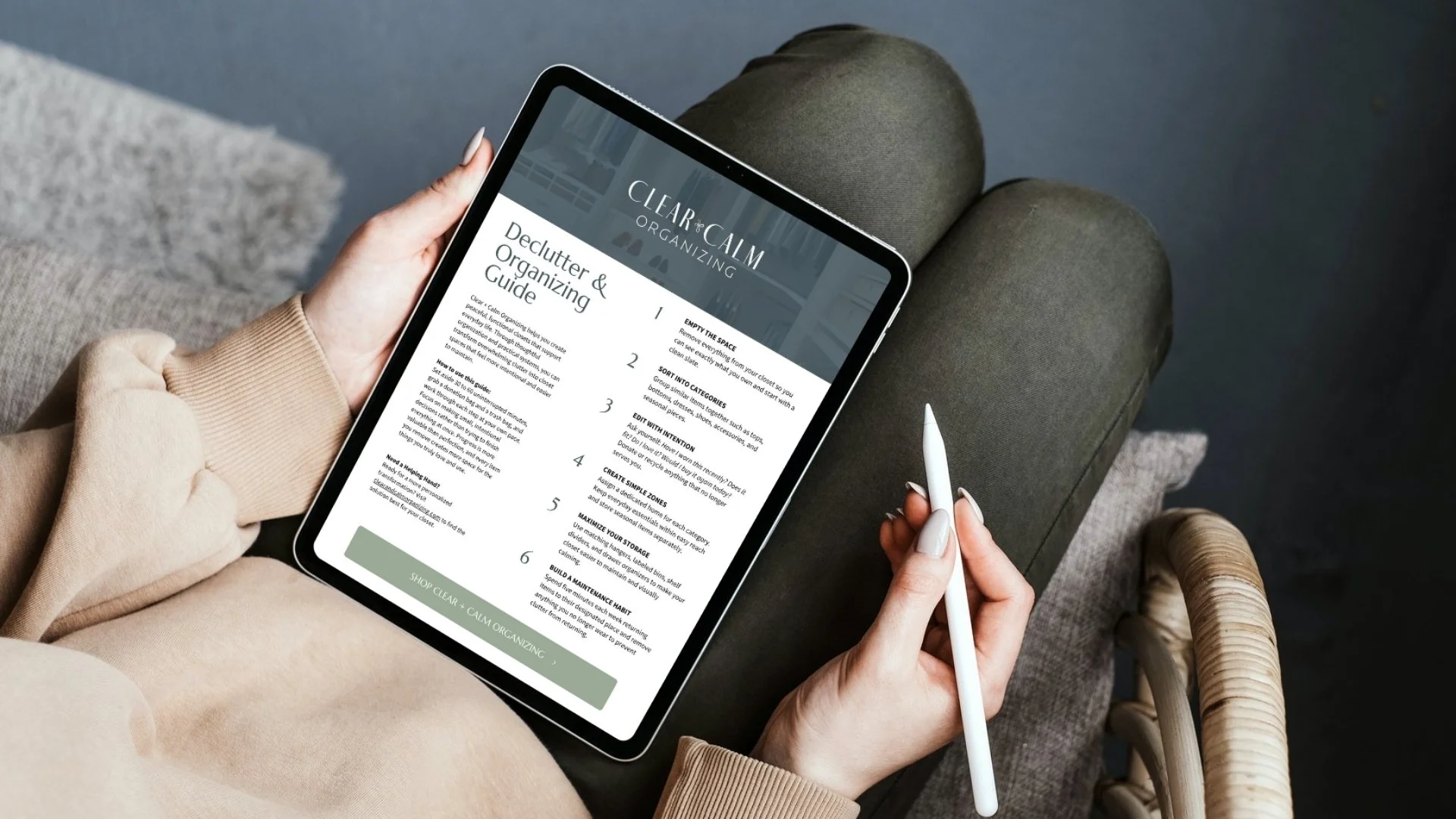 Person sitting on a sofa holding a tablet and stylus, viewing a declutter and organizing guide from Clear & Calm Organizing.