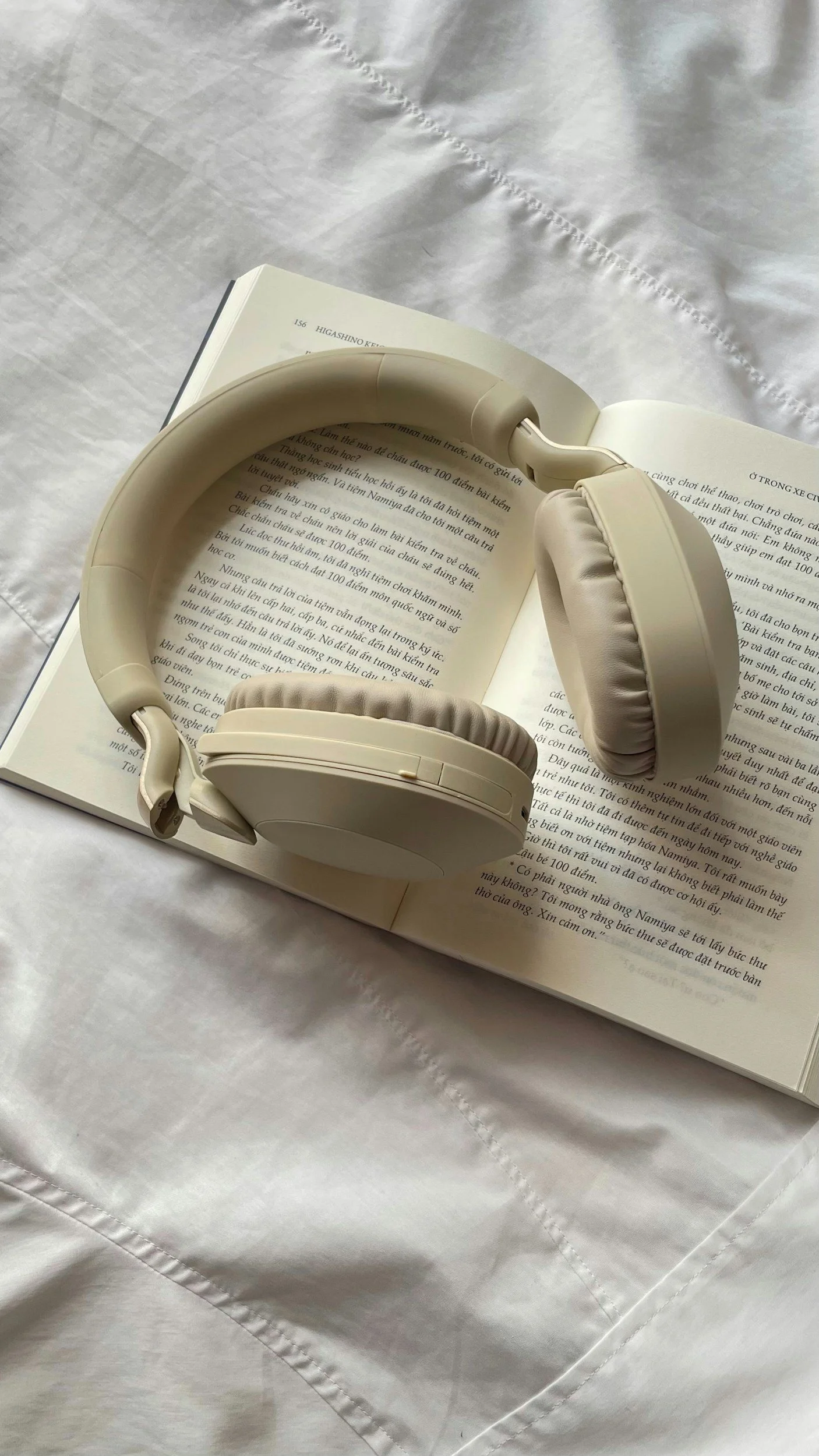 A white pair of over-ear headphones resting on an open book with text, on a white fabric surface.