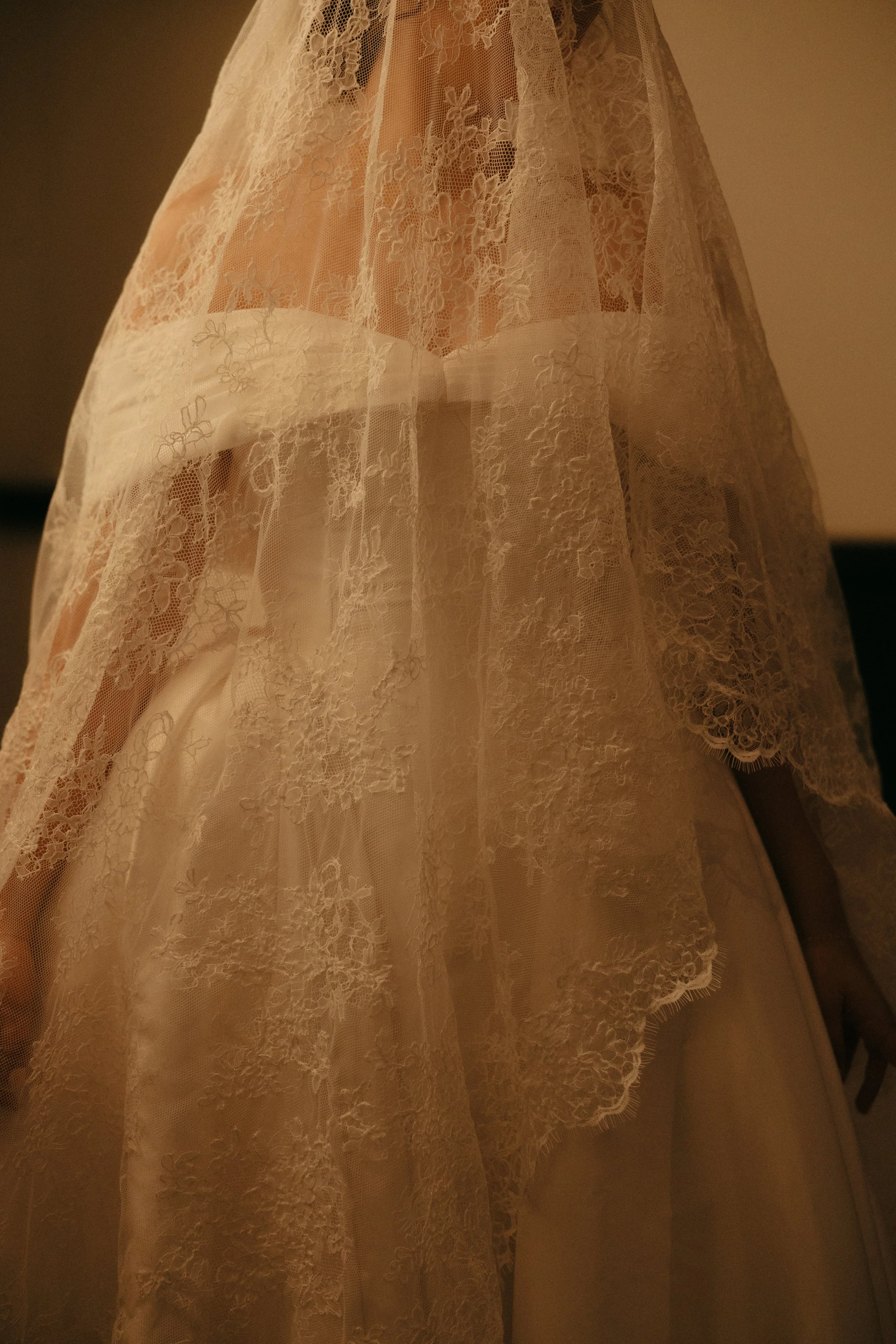 Isabel Marie Photography - Close-up of a sheer, lace fabric with floral embroidery, draped over a person.