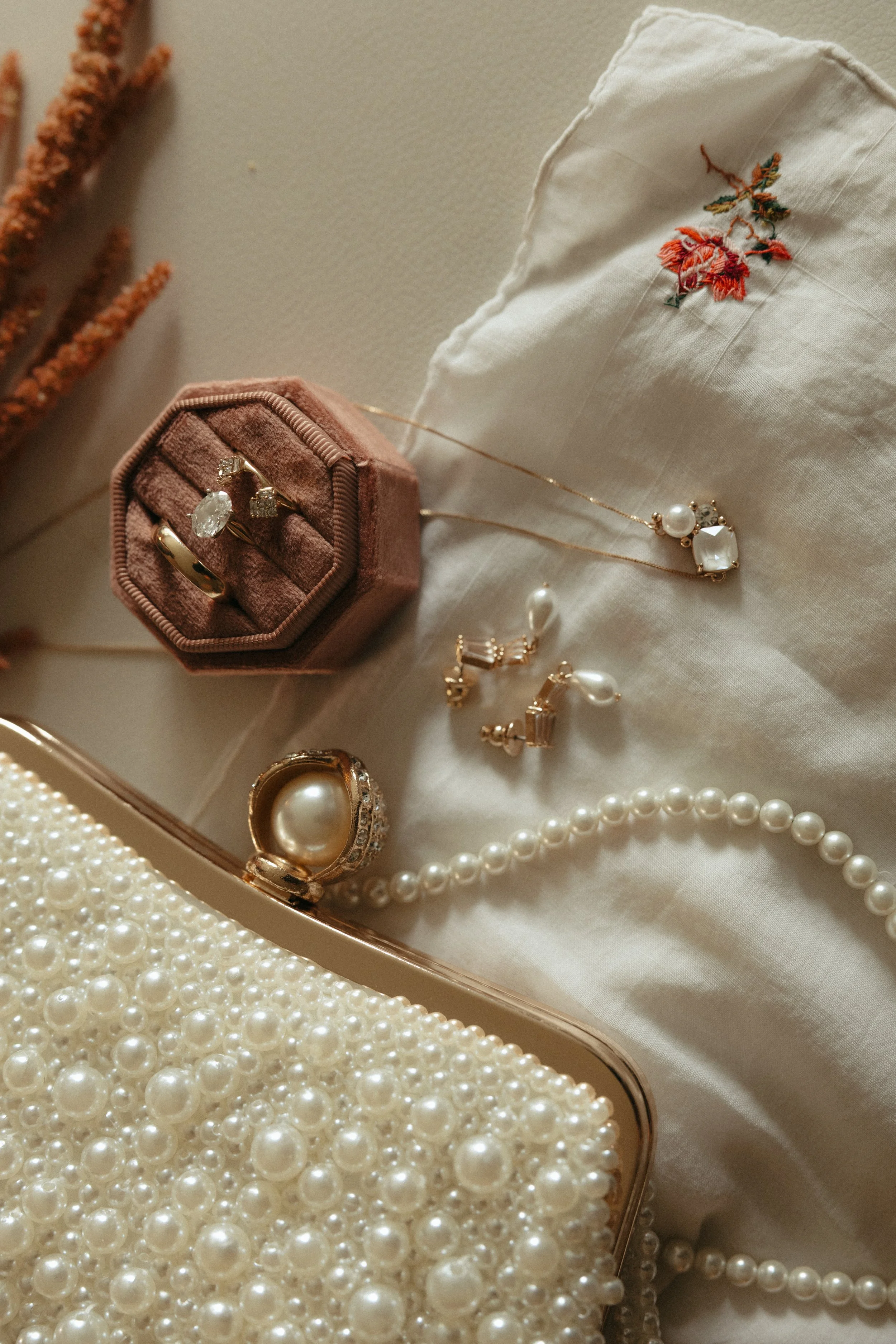 Isabel Marie Photography - Jewelry including a pearl necklace, pearl earrings, rings, a gold and pearl ring, a pendant necklace with pearl and gemstone, all displayed with a pearl-clad clutch bag and a pink ring box with rings inside