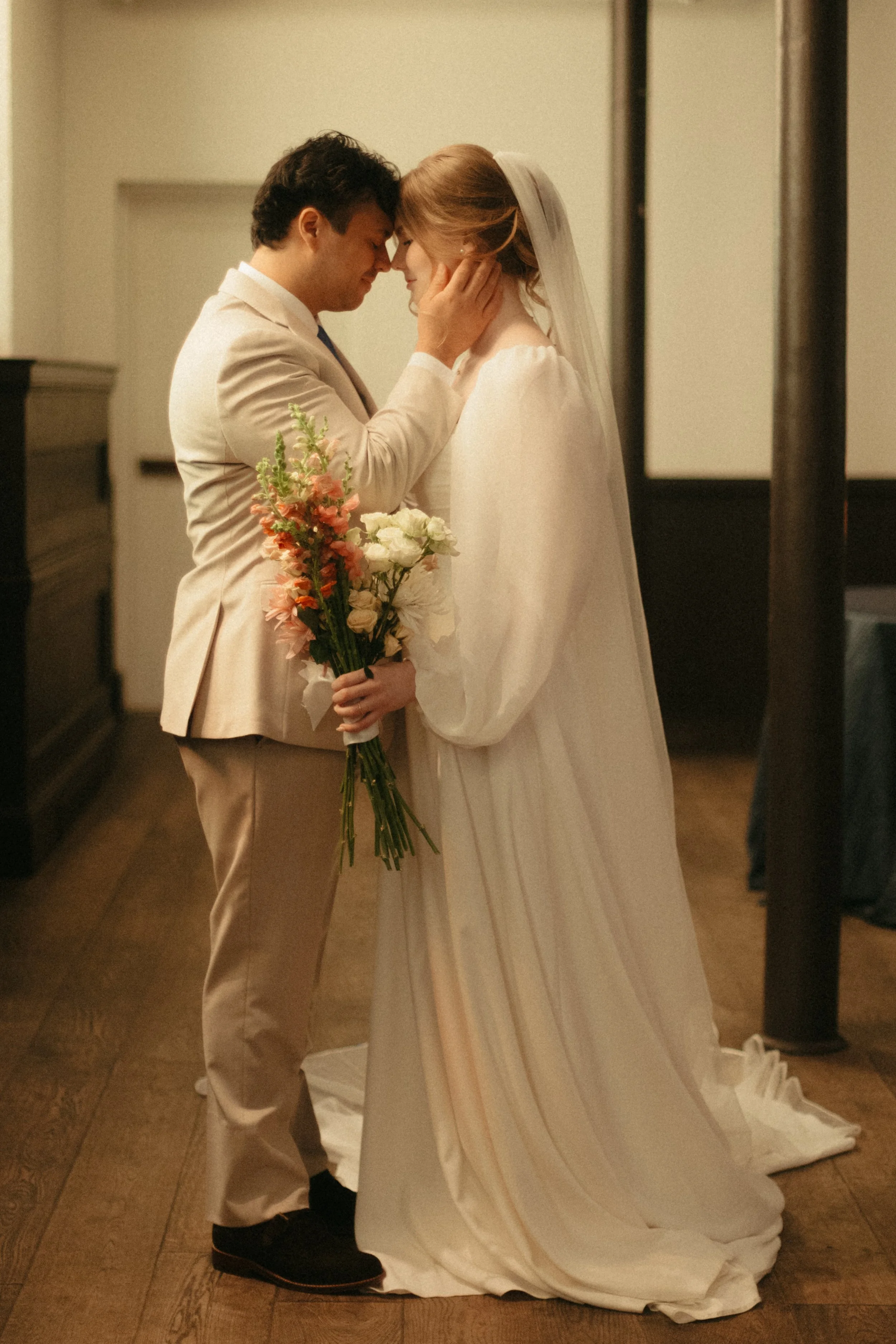 Isabel Marie Photography - A bride and groom share a tender moment, touching foreheads and holding a bouquet of flowers during their wedding ceremony.