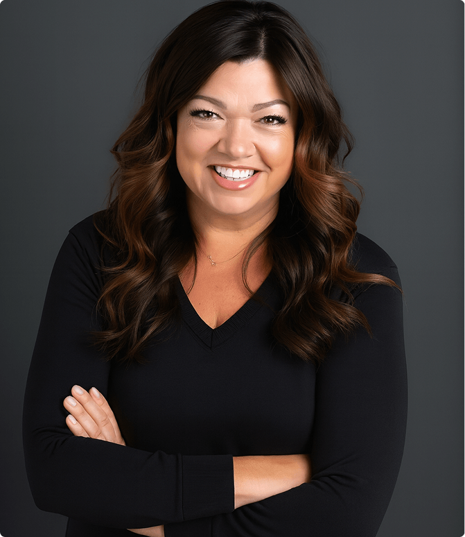 Smiling woman with long wavy brown hair wearing a black top, standing against a dark gray background.