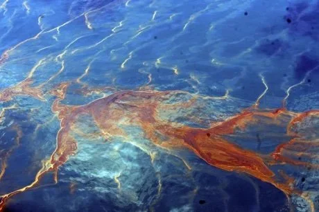 A close-up image of a rusty metal object partially submerged in water, with reflections and ripples on the water surface.