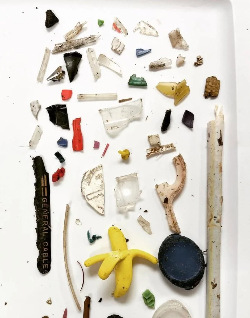 Various small, broken pieces of plastic, glass, and other debris scattered on a white surface, including a small yellow plastic banana, a black circular object, and a white straw.