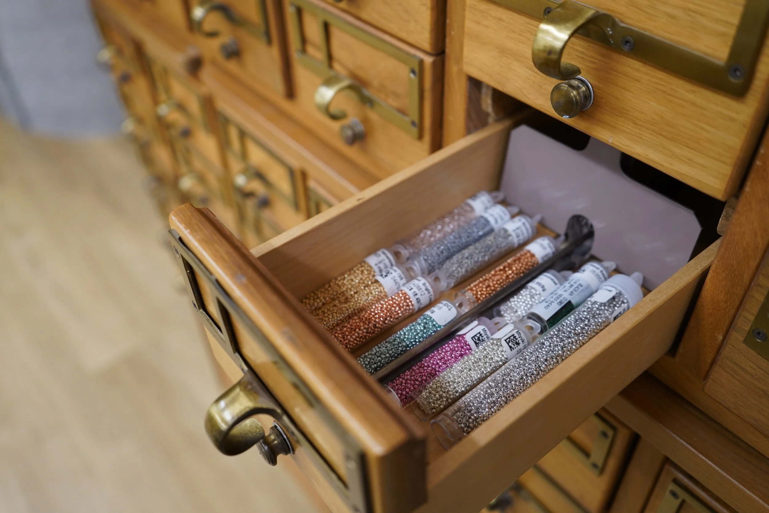 A wooden drawer partially open, showing tubes of small rhinestones or beads in various colors laid out inside.