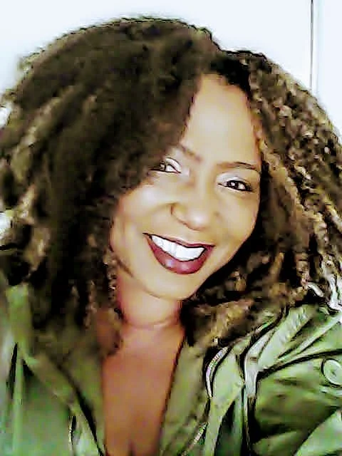 Smiling woman with curly hair and wearing a green jacket.