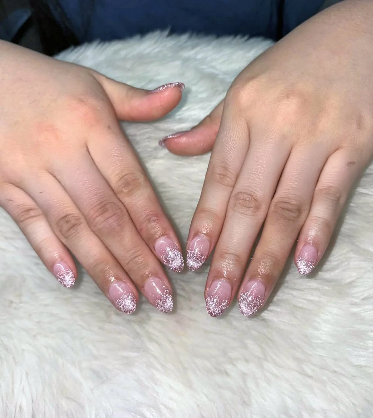 Hands with glittery pink French manicure resting on a white furry surface.