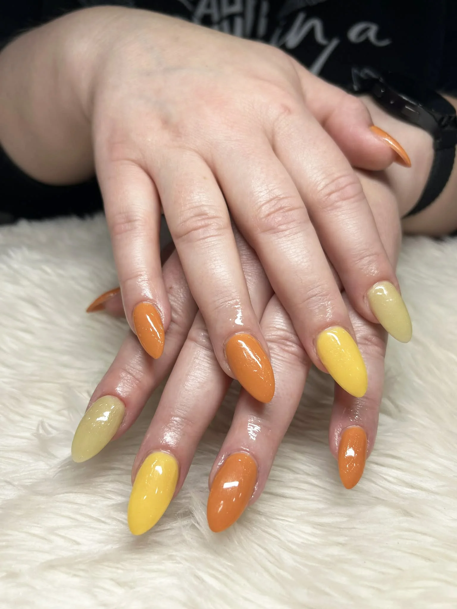 Hand with colorful yellow and orange almond-shaped nails resting on a furry surface.