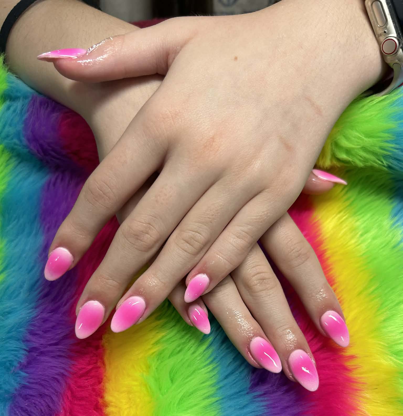 Hands with pink and white ombre acrylic nails resting on colorful rainbow tie-dye fabric.