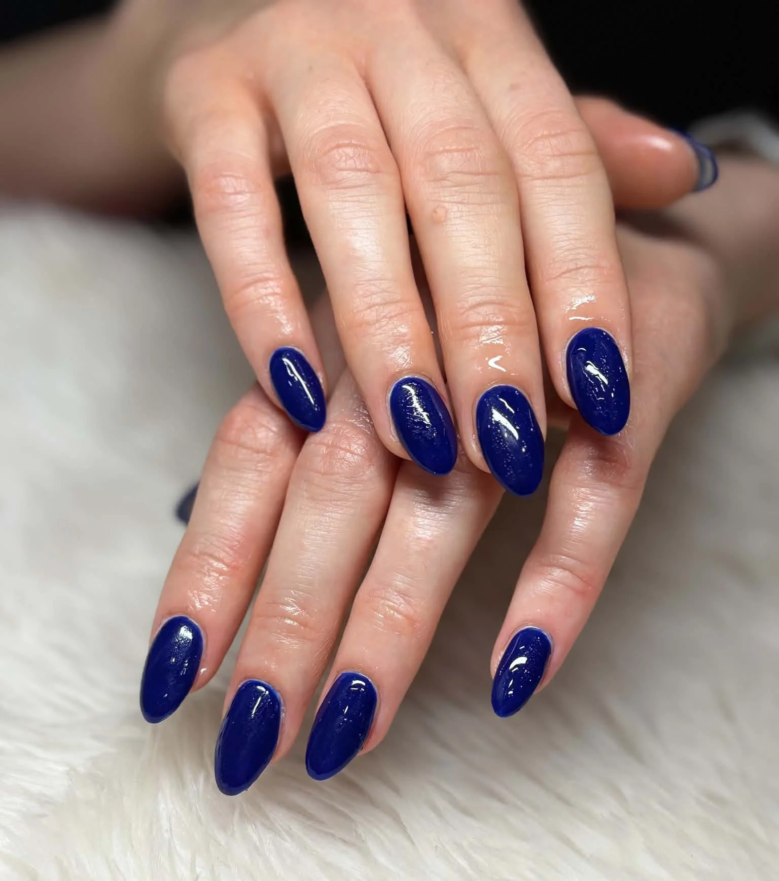 Close-up of hands with manicured nails painted in dark blue, resting on a soft white surface.