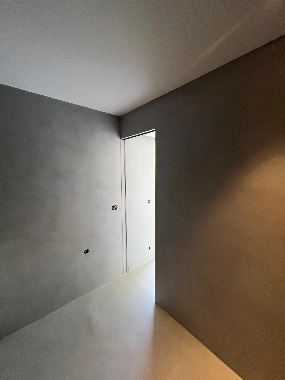 Mur en béton ciré gris et porte à galandage dans un couloir