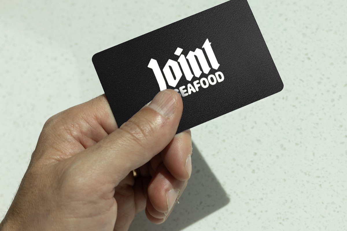 A hand holding a black card with white text that reads 'joint SEAFOOD' against a light speckled background.