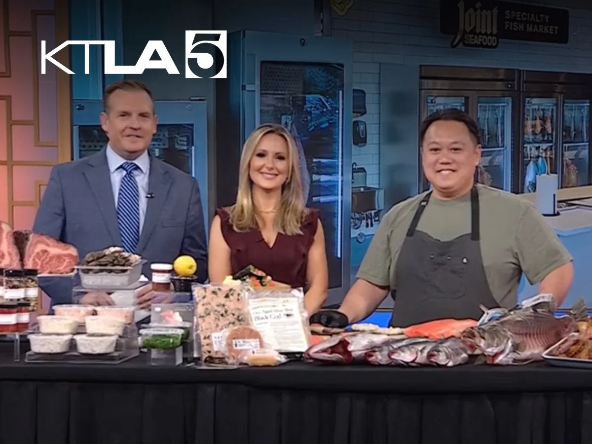 Three people standing behind a table with seafood and other food items displayed, on a television set with the logo KTL A5 in the top left corner.