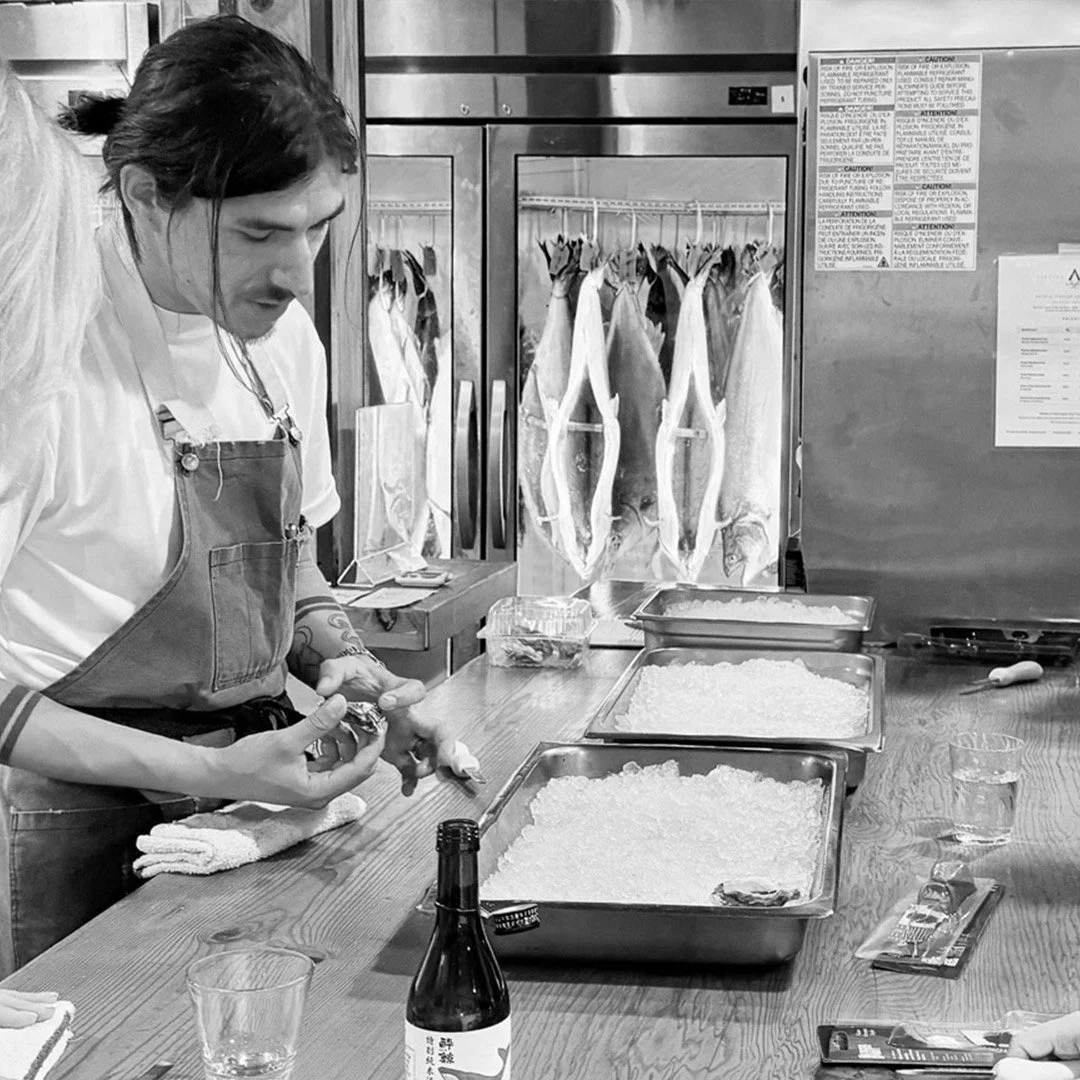 A chef preparing fish in a kitchen with hanging fish on a rack in the background.