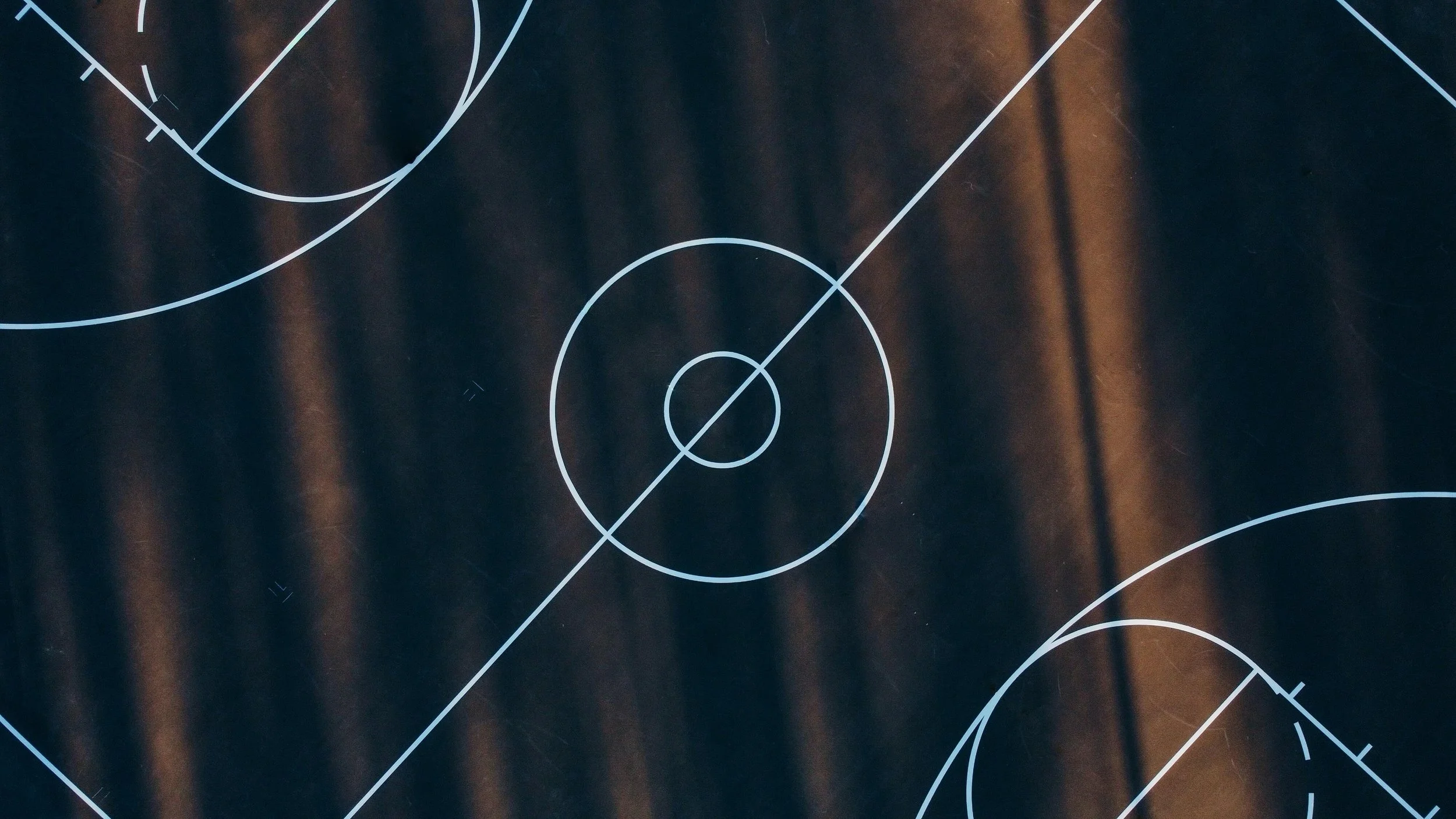 A black basketball court with white markings, including a center circle, three-point arcs, and boundary lines.