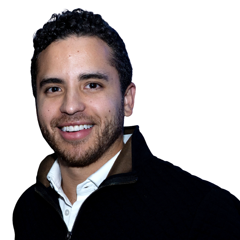 A young man with dark curly hair and a beard, smiling, wearing a white shirt and a dark jacket.