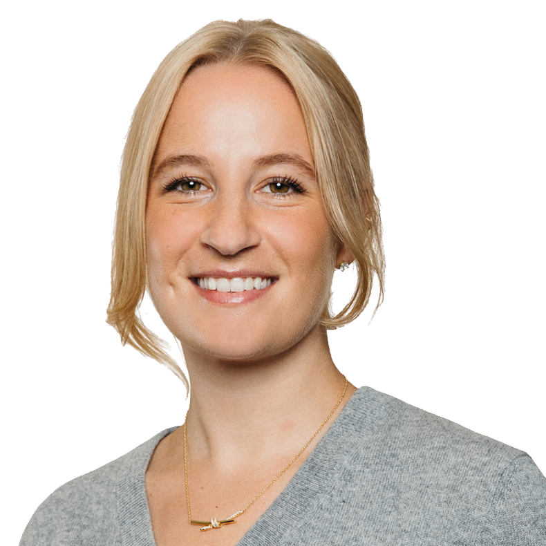 A smiling blonde woman with blue eyes wearing a gray top and a gold necklace.