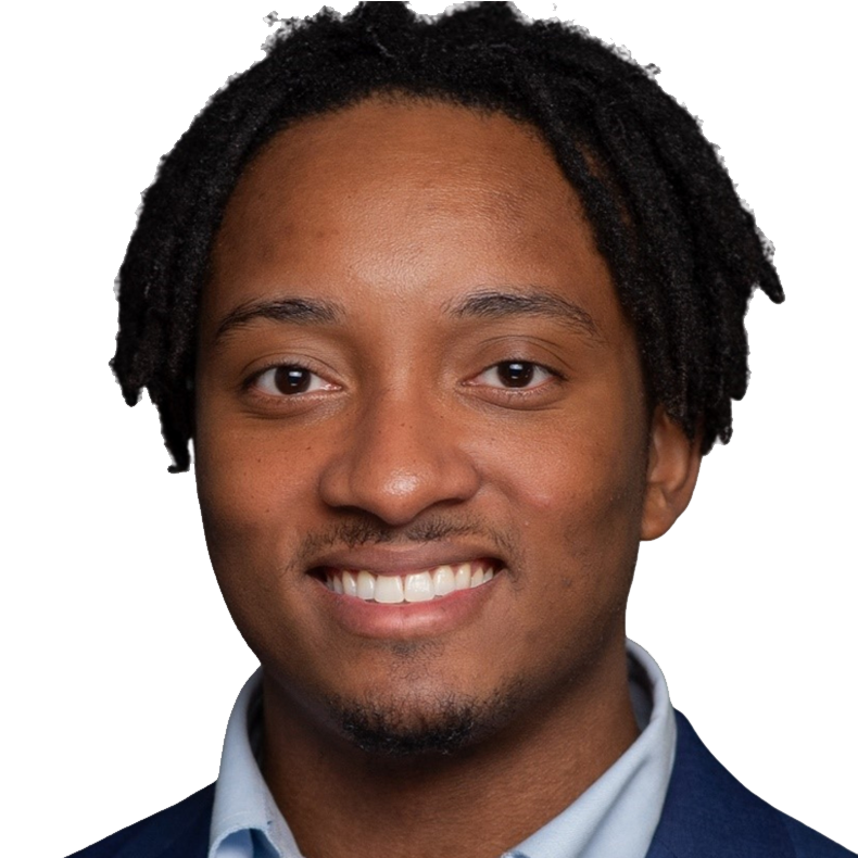 A young man with dark curly hair, smiling, wearing a light-colored shirt and a dark blazer.