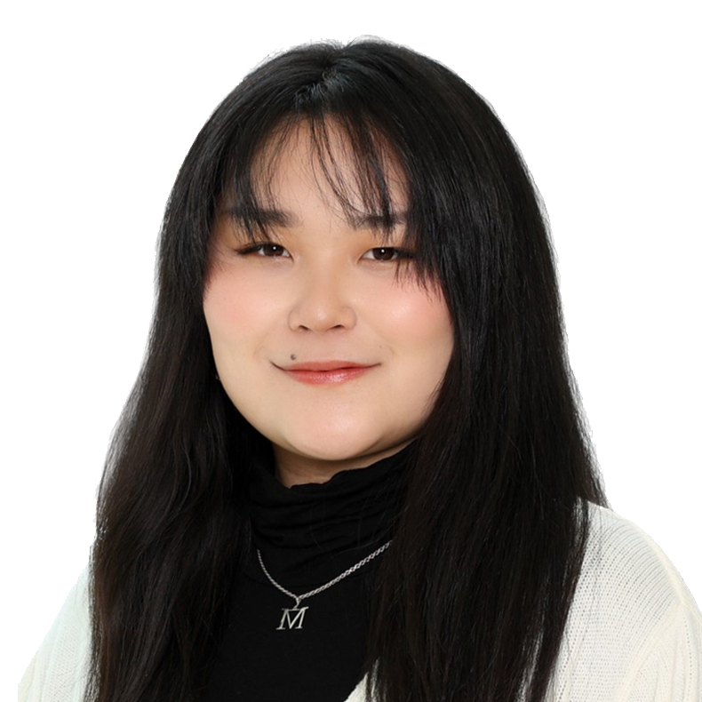 A woman with long black hair wearing a black turtleneck and white cardigan, smiling, with a silver necklace with an 'M' pendant.