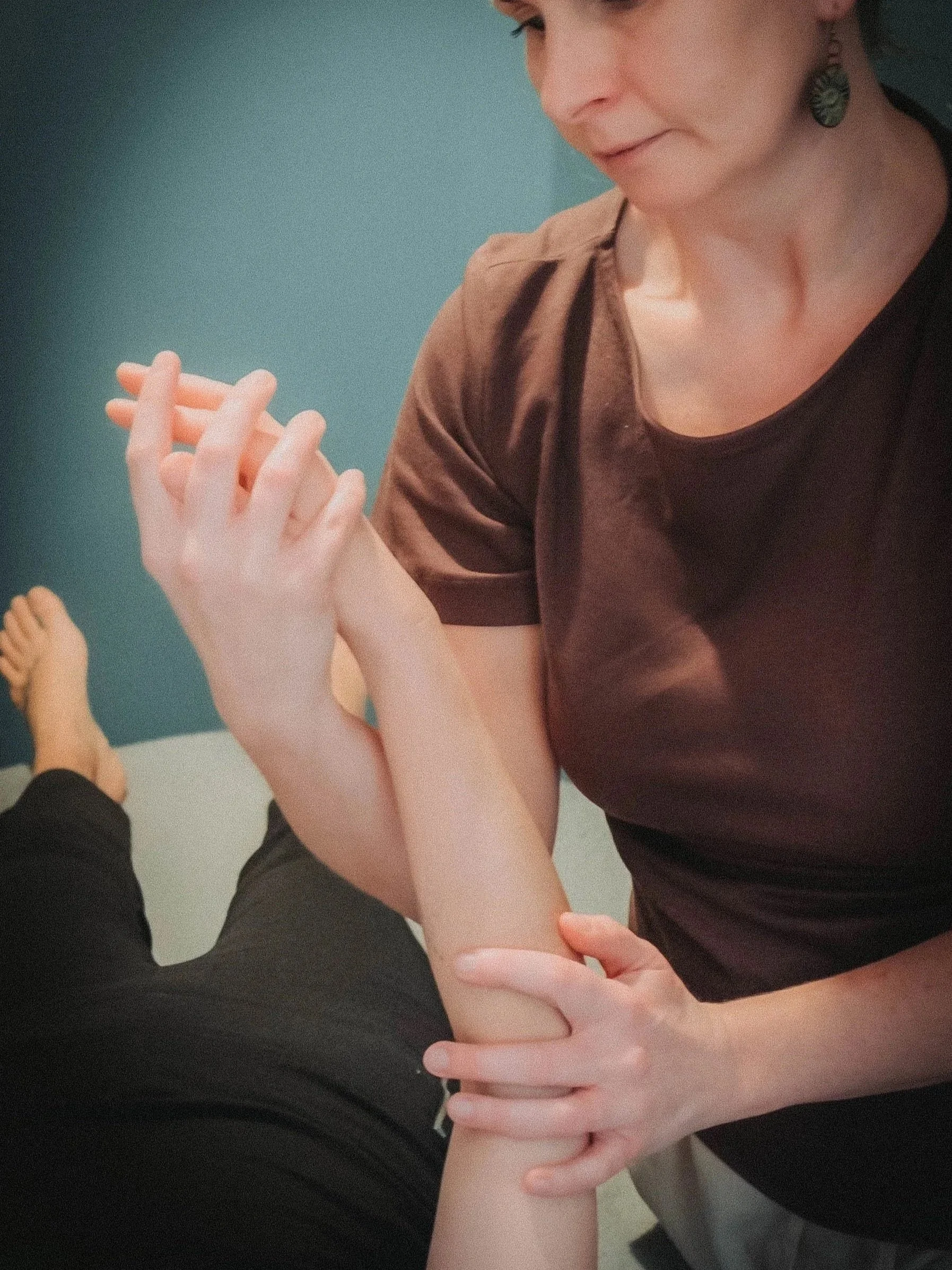 A woman with earrings and short dark hair is seen smiling while holding hands with a person dressed in black. The woman's hands are gently gripping the person's arm.